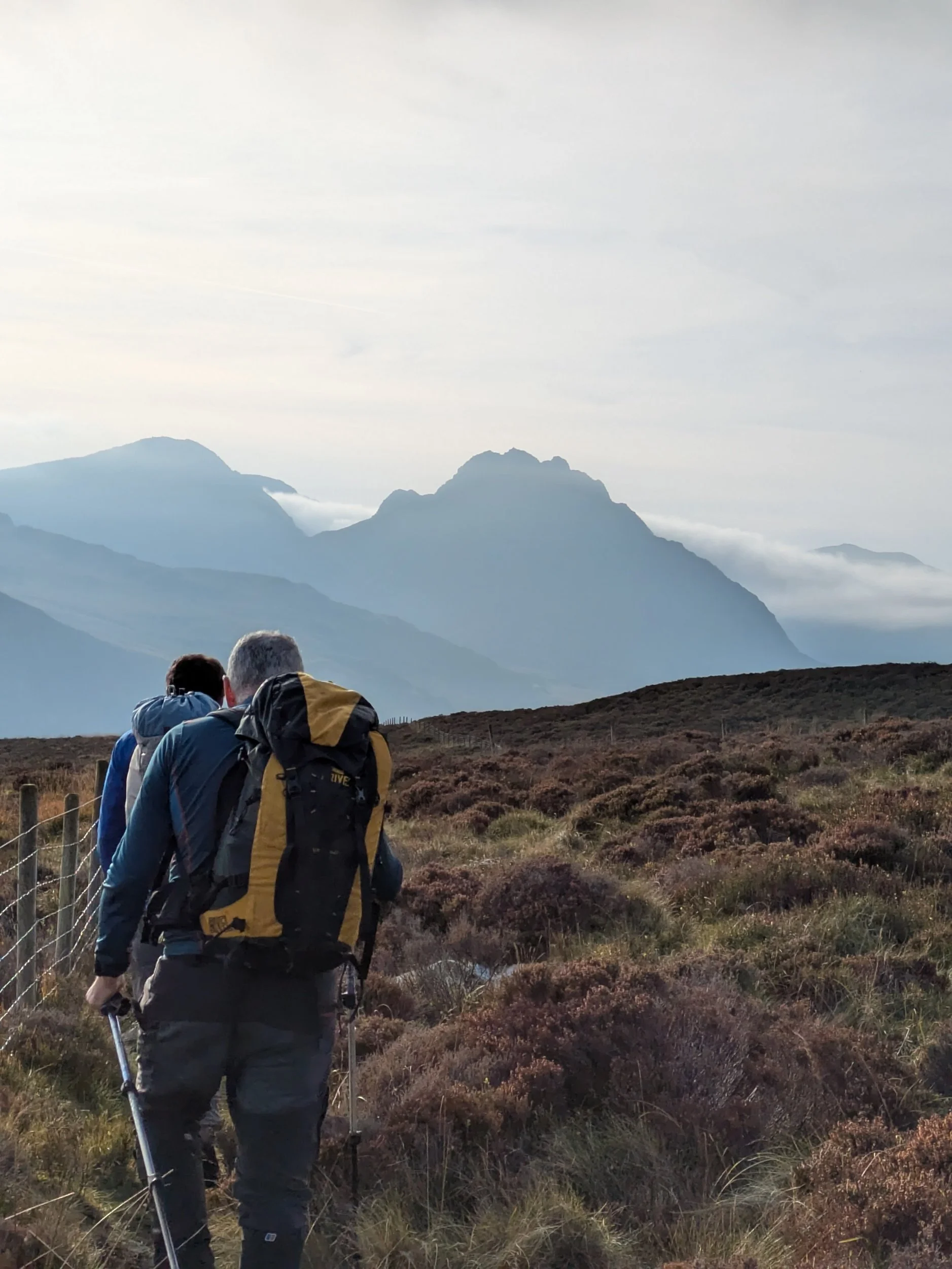 Hikers walking on a trail through mountainous terrain with cloudy skies.
