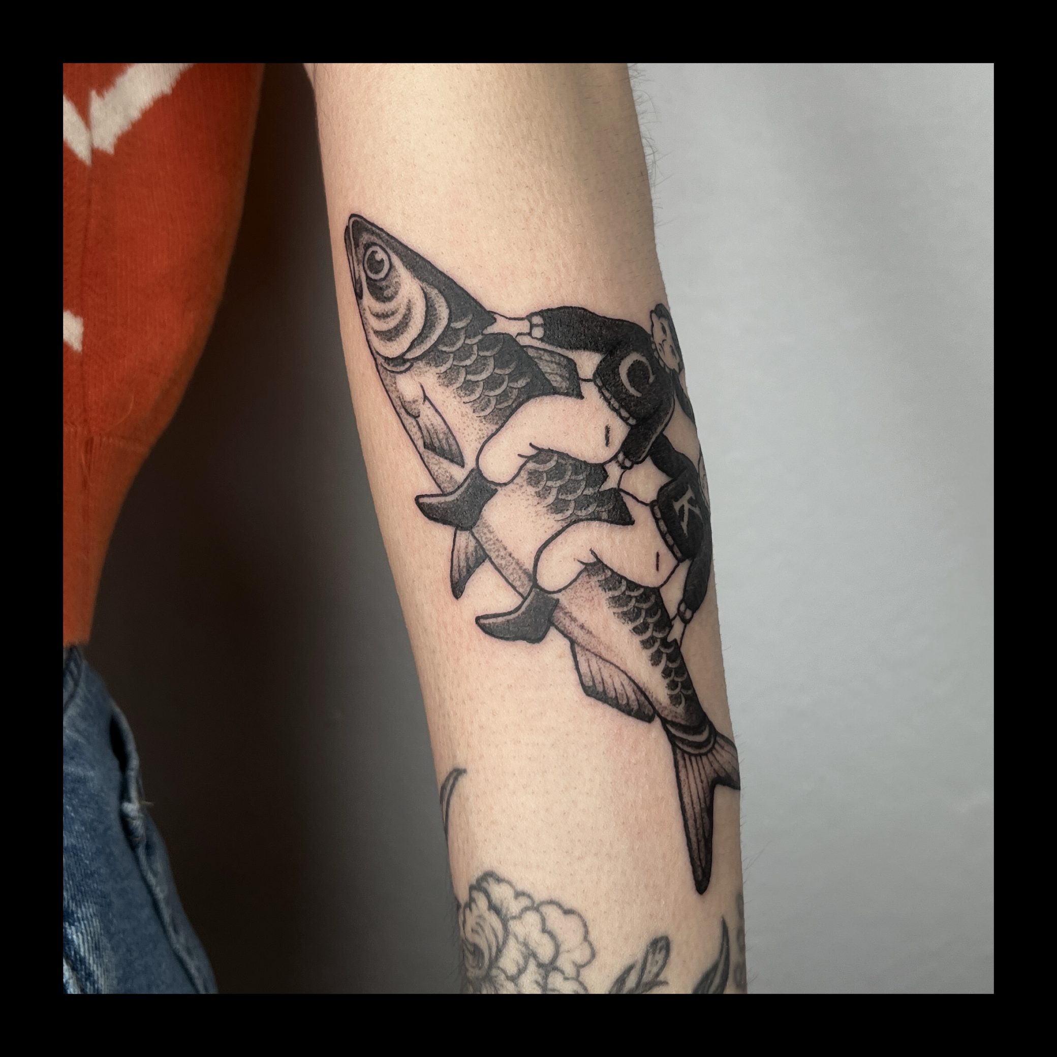 Tattoo of a fish and a mermaid on a person's arm.