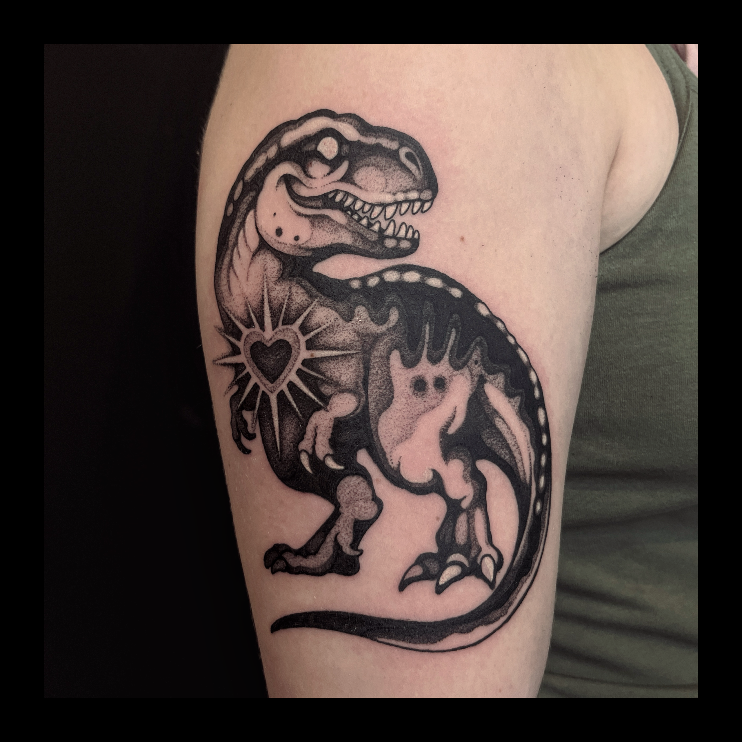 Black tattoo of a T. rex dinosaur on person's upper arm.