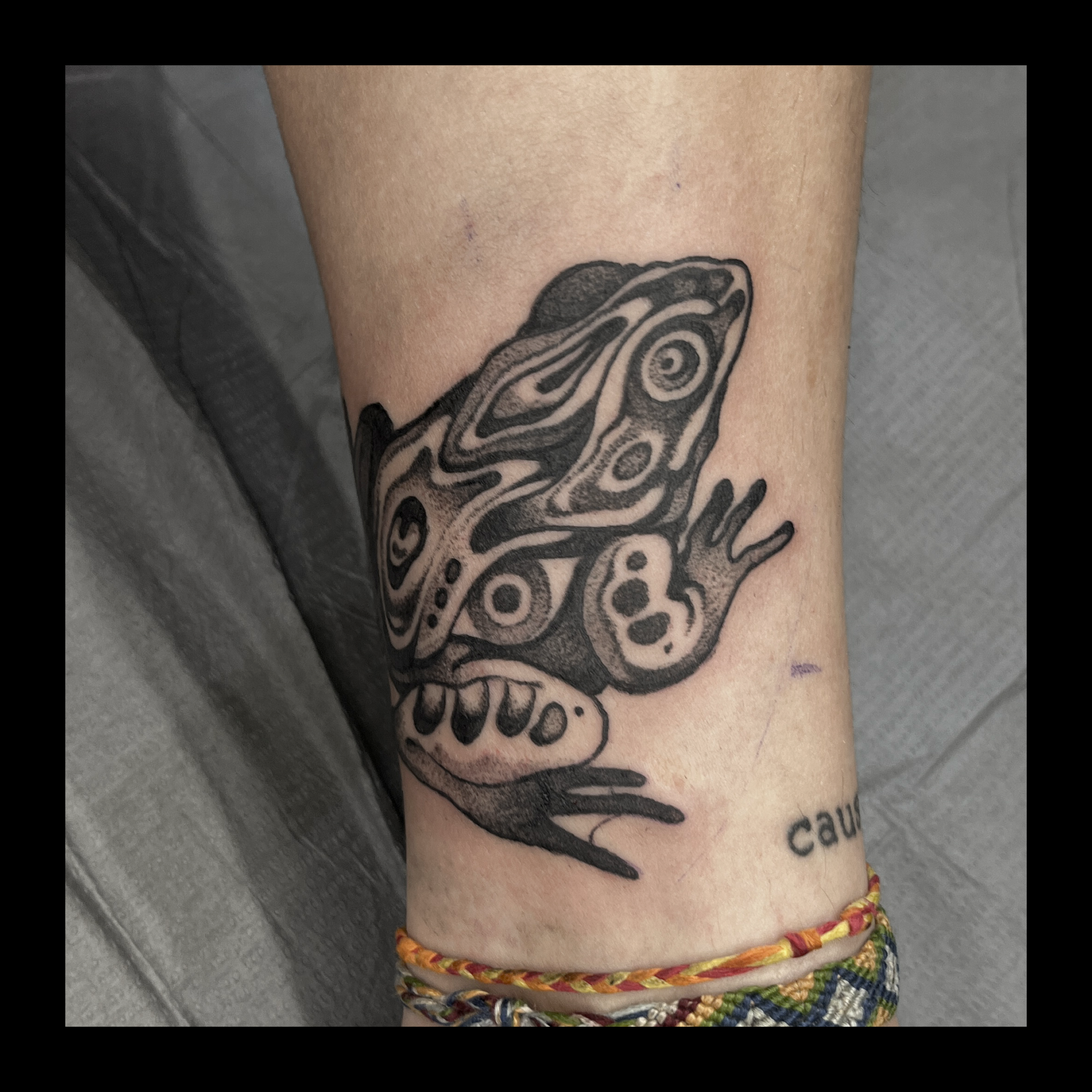 A tattoo on a person's forearm featuring a stylized eye with swirling patterns, accompanied by text underneath.