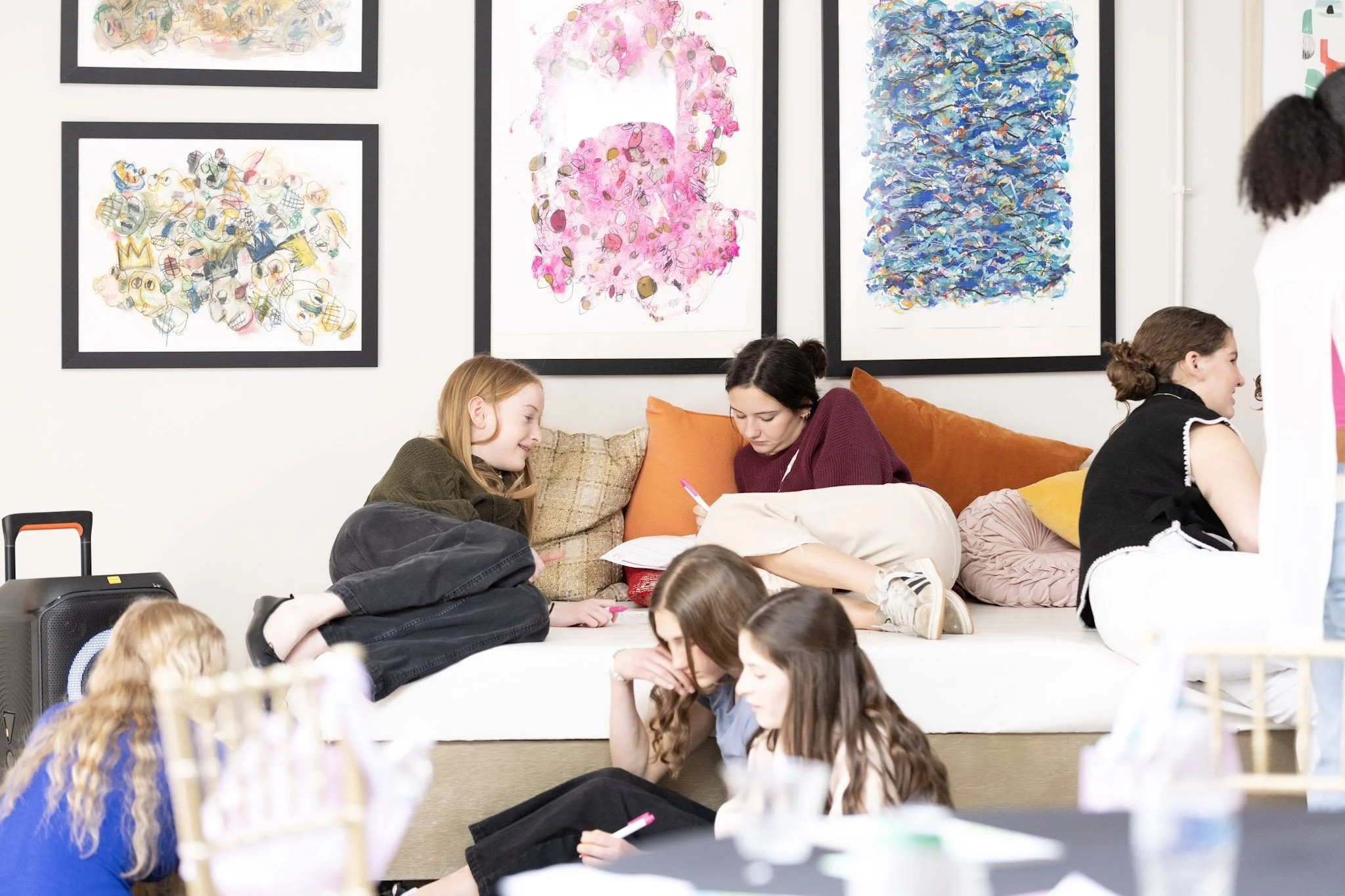 People sitting on floor in a room with colorful abstract artwork on the wall.