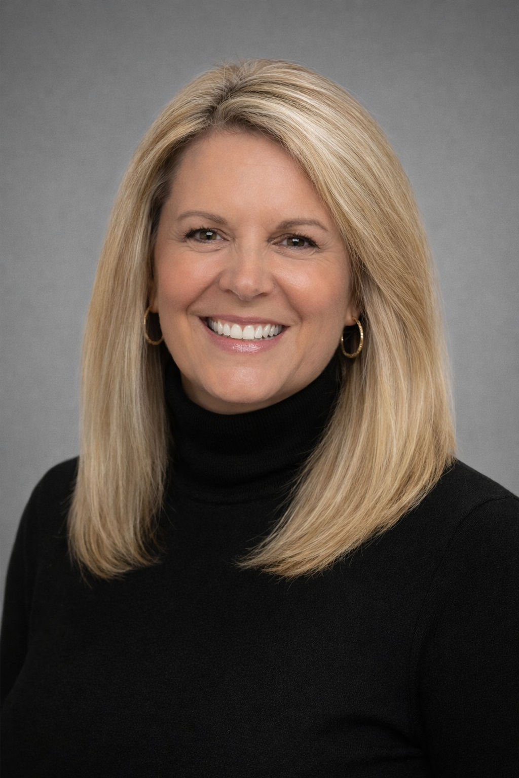 Headshot of a smiling woman with blonde hair, wearing a black turtleneck and hoop earrings, against a gray background.