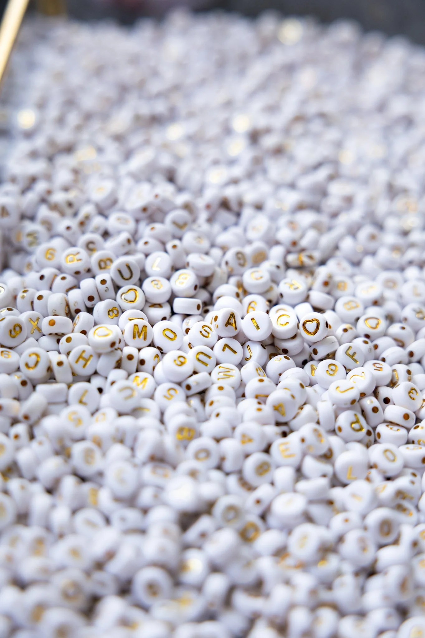 Close-up of numerous small white beads with gold letters and symbols, some forming words and hearts.