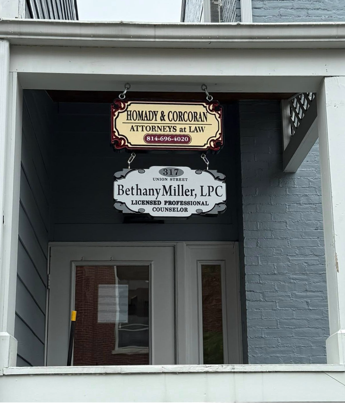 Signs for law offices displayed on a porch, including Homady & Corcoran Attorneys at Law and Bethany Miller, LPC, Licensed Professional Counselor.