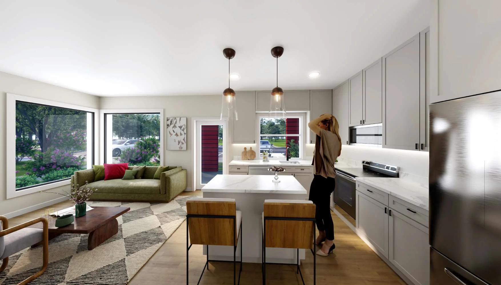 Modern kitchen and living room with large windows, green sofa with red and green pillows, kitchen island, woman standing by the sink, and outdoor greenery visible through windows.