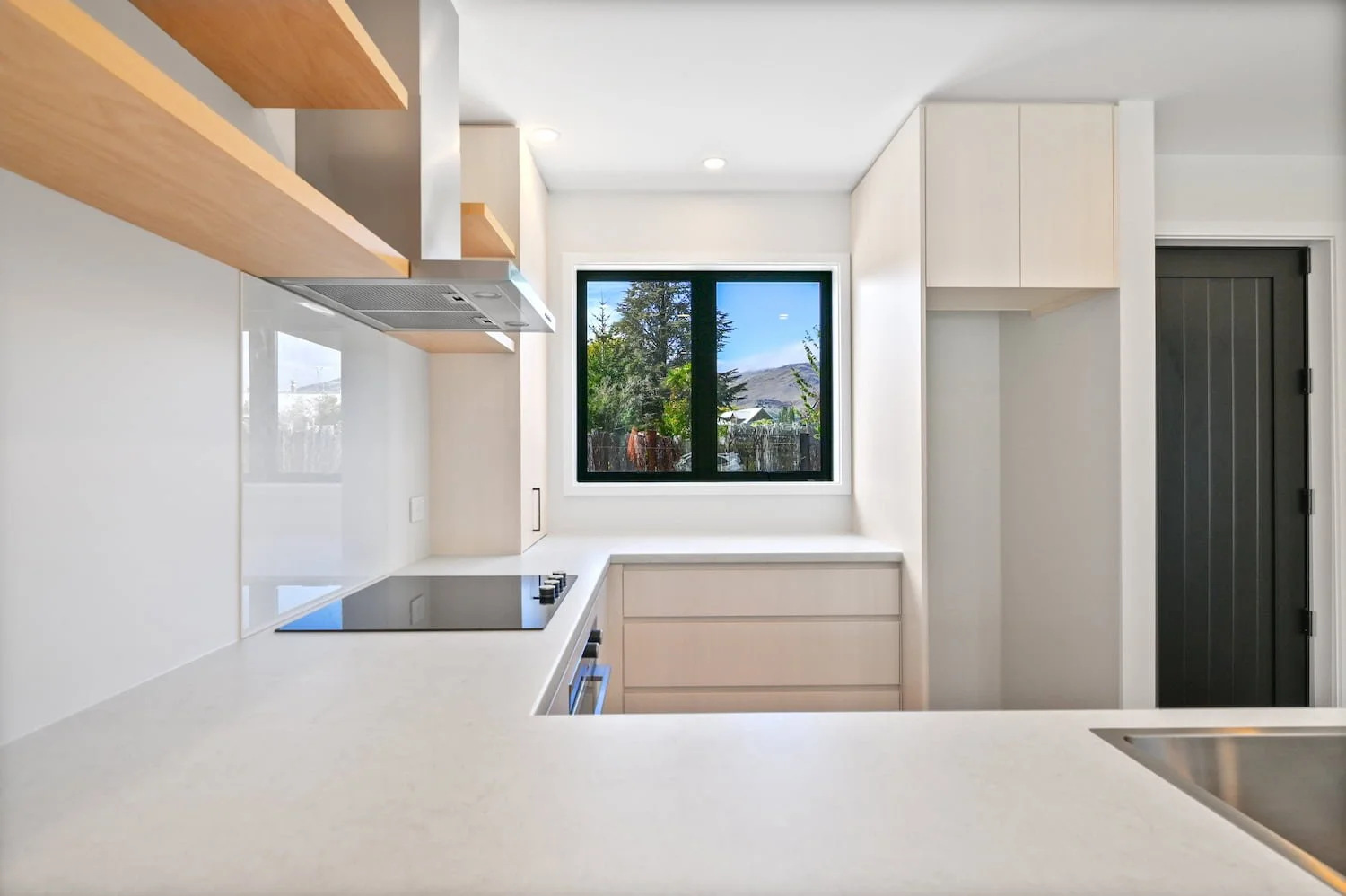 Contemporary kitchen in a Pisa Vistas townhouse with stone benchtop, induction cooktop, timber open shelving and a window with garden views.