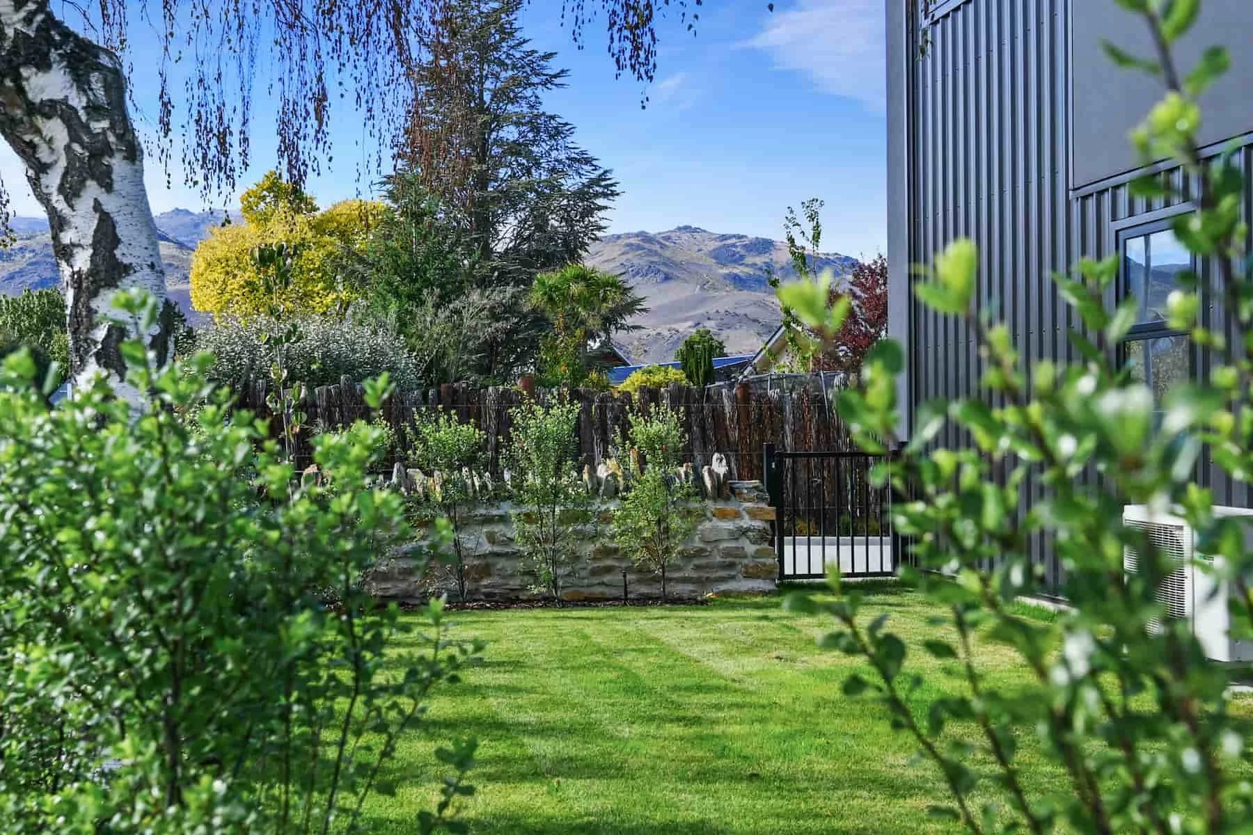 Landscaped garden at a Pisa Vistas townhouse, with lawn, established trees, schist stone fencing and mountain views beyond.