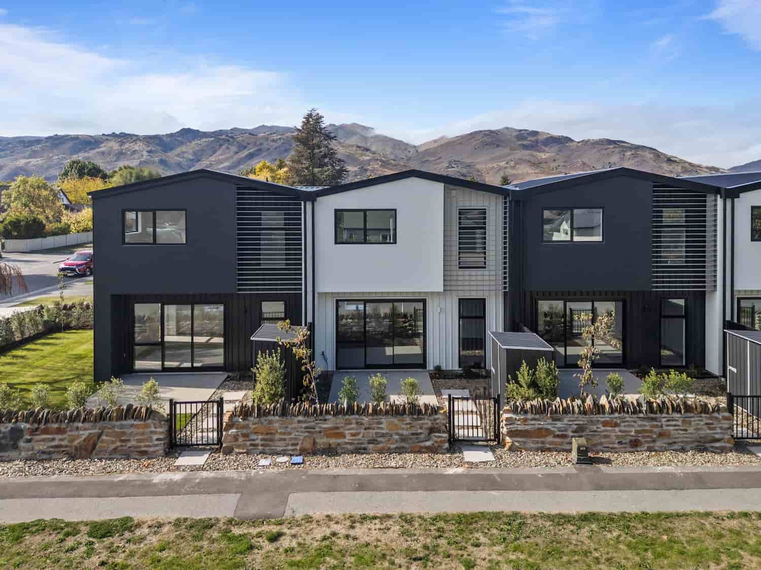 Modern two-storey townhouse at Pisa Vistas in Cromwell, with dark cladding, louvre shutters, schist stone boundary wall and mountain views.