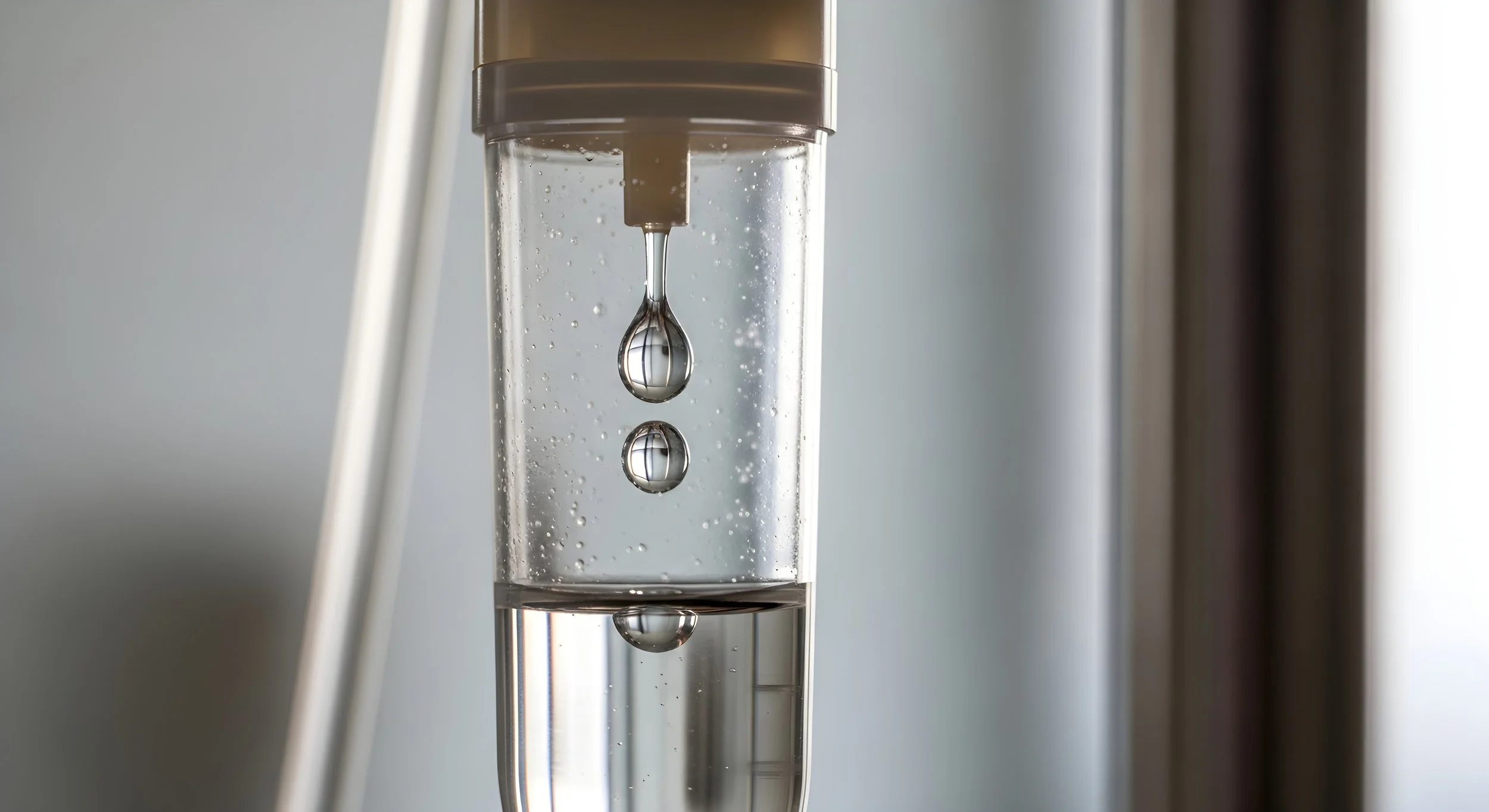 A close-up of an indoor water faucet with water droplets falling into a glass container beneath it.