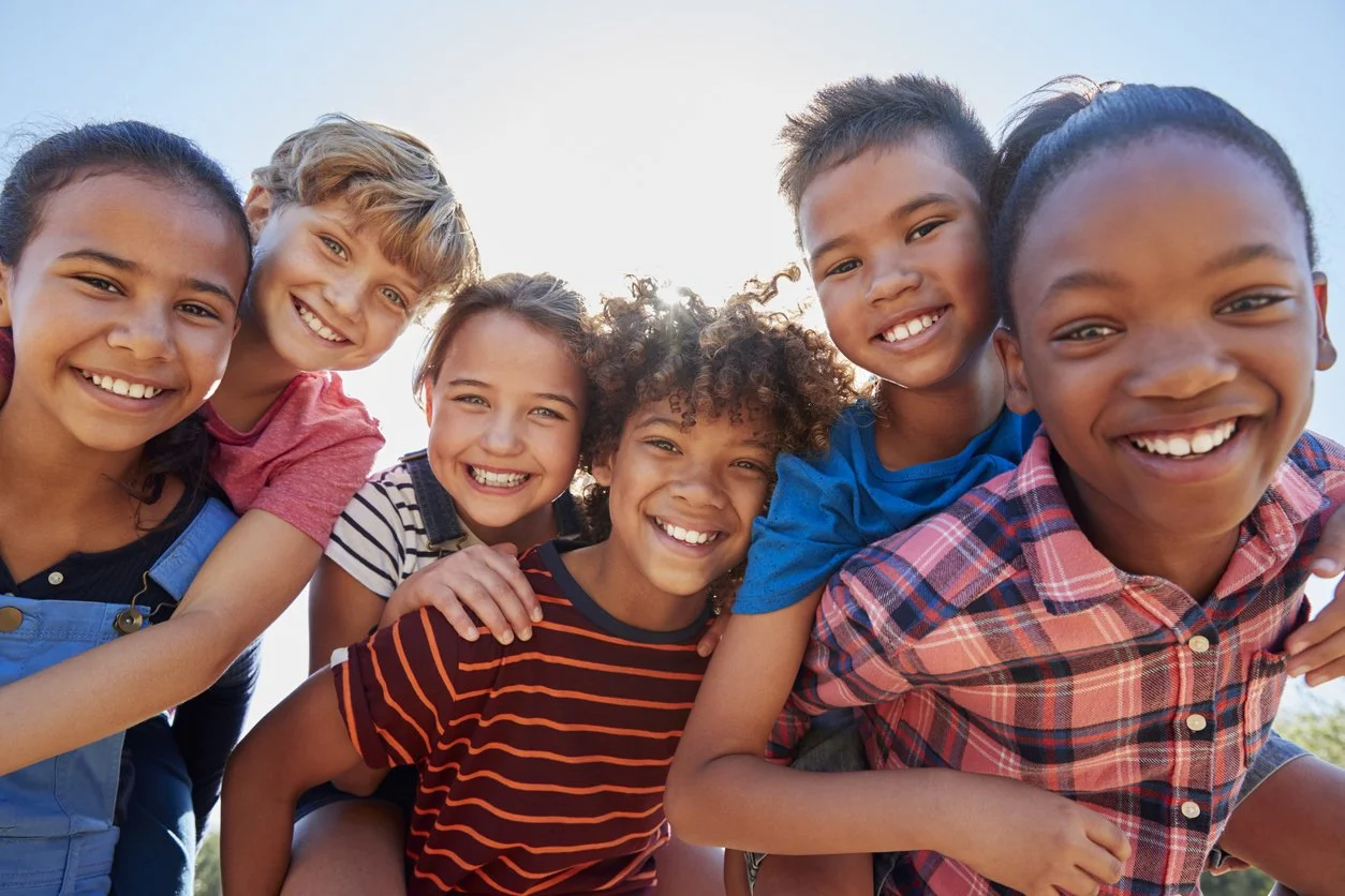 Group of six diverse children smiling and having fun outdoors, all with improved social skills after receiving speech therapy from a school contract speech therapist in Michigan.