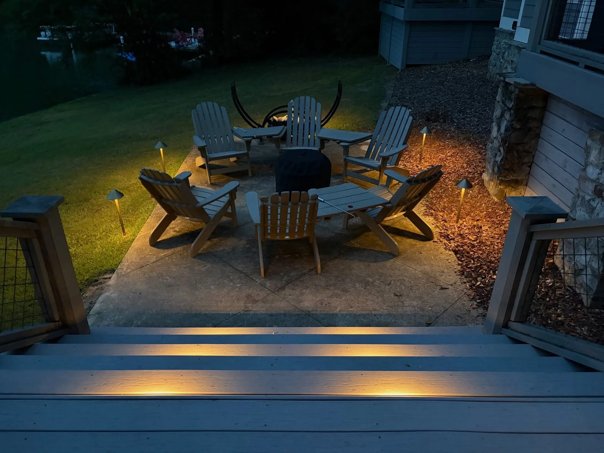 A beautiful landscaped outdoor seating area with lighting and Adirondack chairs