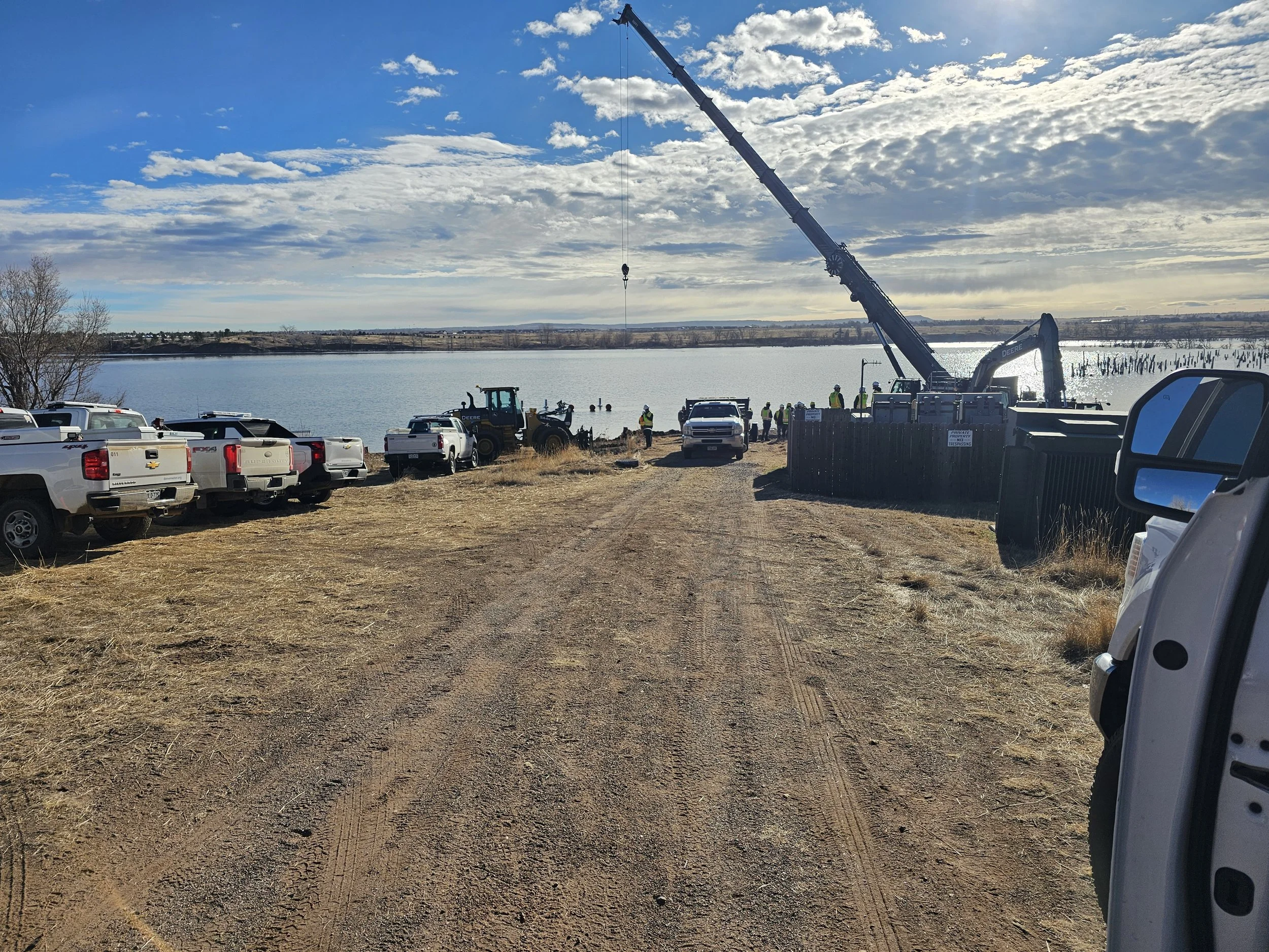 Construction site by a large body of water with a crane, trucks, workers, and equipment.