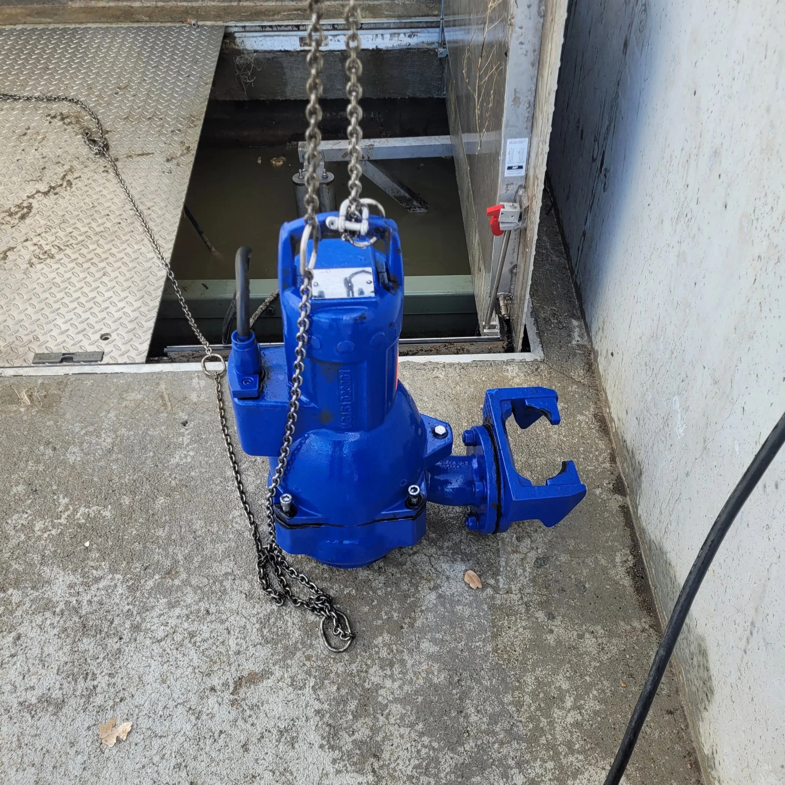 Blue hydraulic lift in a construction area with chains hanging from it, next to a metal platform and a white wall with some peeling paint.