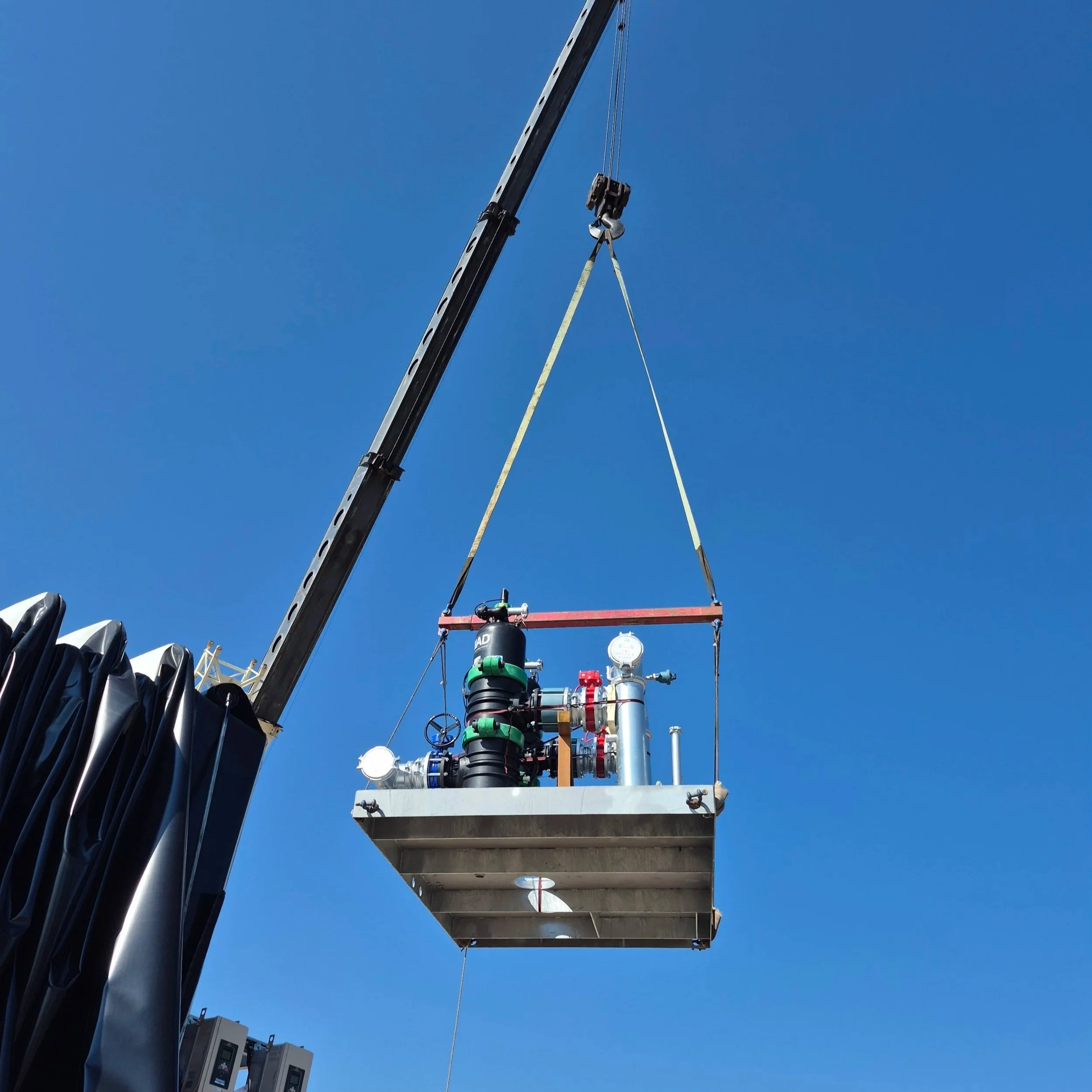 An industrial or utility platform with various pipes, valves, and instruments installed on it, elevated against a clear blue sky, possibly part of a construction or maintenance site.