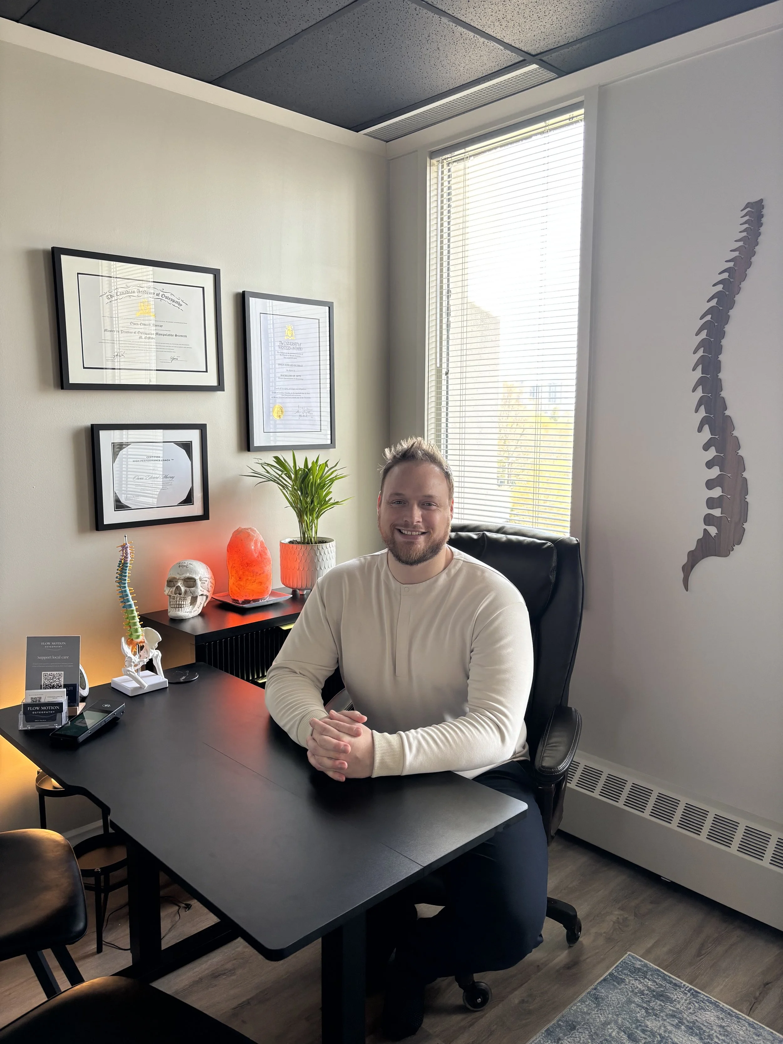 Owen Murray, top-ranked Osteopath at Flow Motion Osteopathy in London, Ontario, Canada. Osteopathy with Owen is located at 111 Waterloo Street in London. Seen here as a large bearded man sitting at his desk in his Osteopathic clinic.