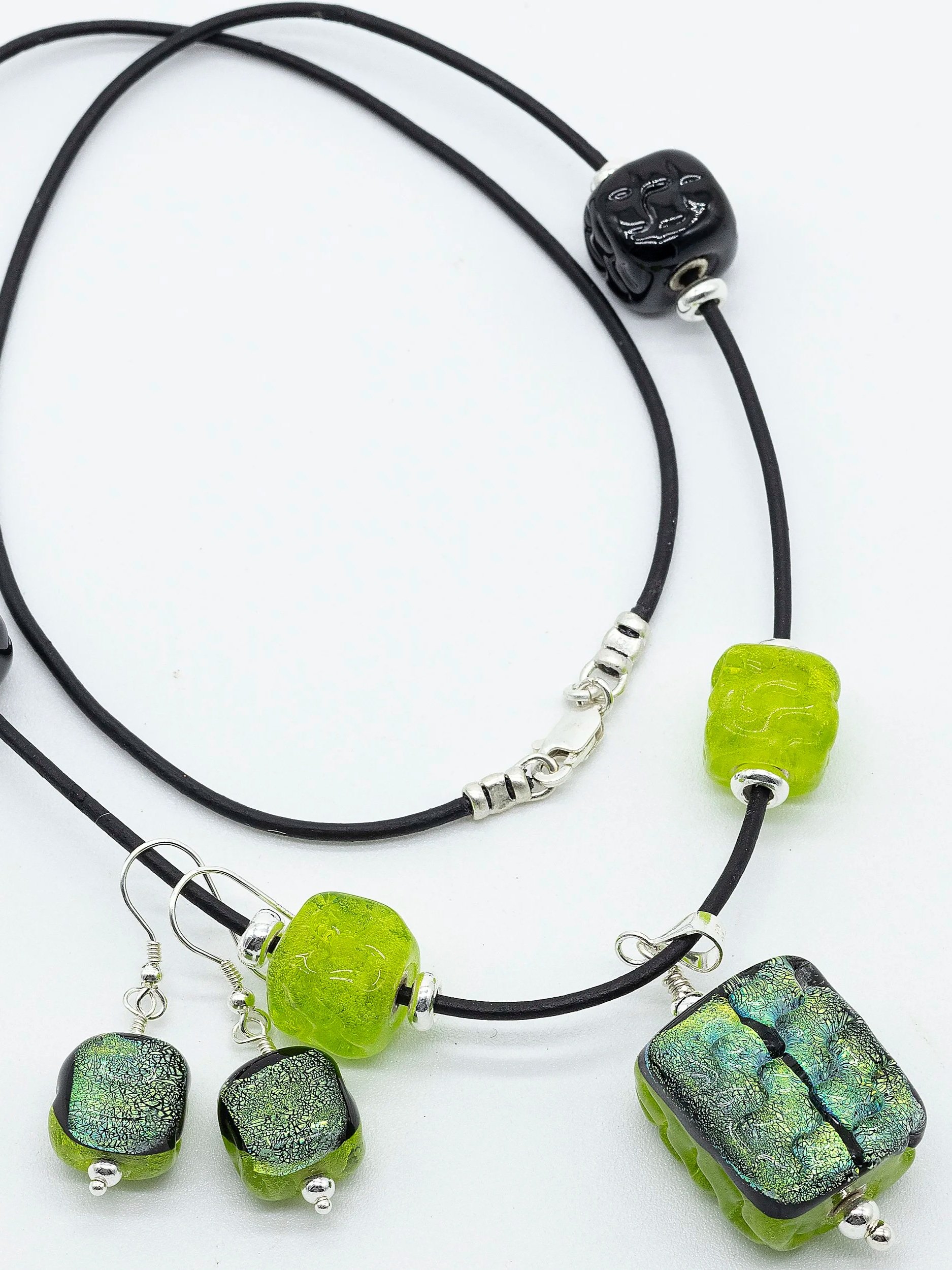 Bijoux en verre vert et noir avec des cordons noirs, comprenant des pendentifs rectangulaires et ronds, certains avec un motif de fissure dans le verre.