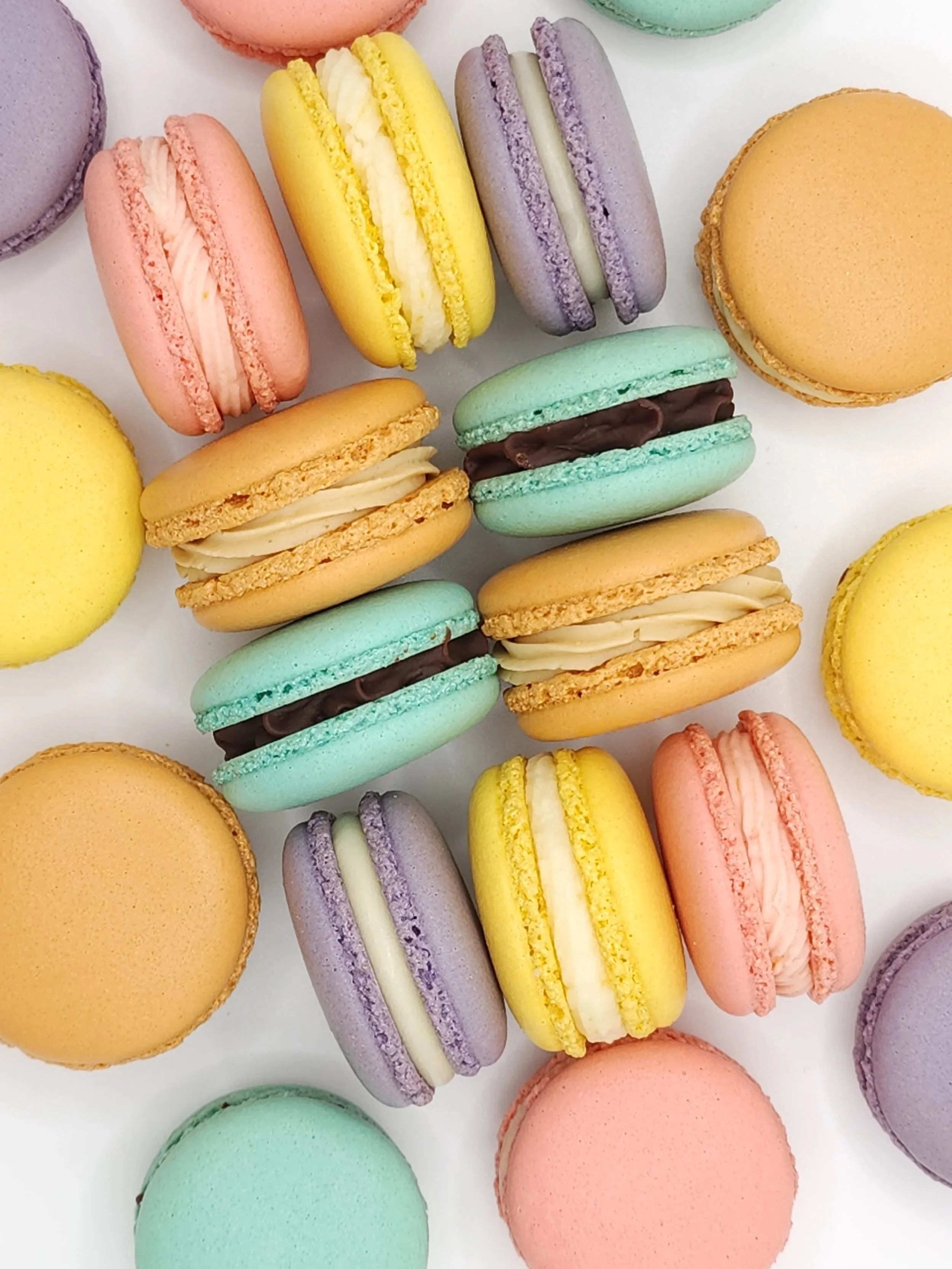 Une collection de macarons de différentes couleurs et saveurs, disposés sur une surface blanche.