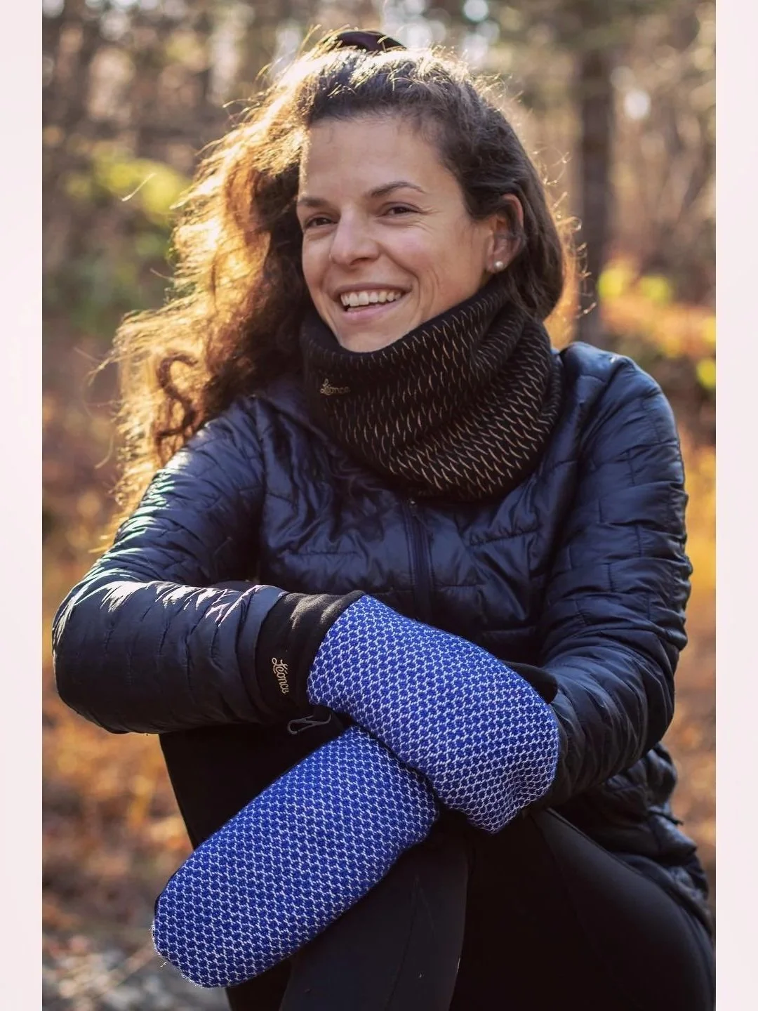 Femme souriante portant un vêtement chaud en plein air, avec un fond forestier en automne.