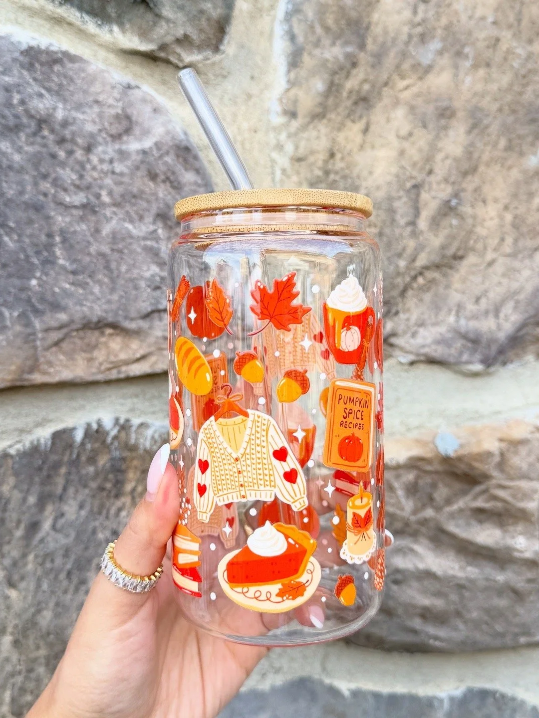 Verre en verre transparent avec des dessins de thèmes automnaux, comme des feuilles d'érable, des citrouilles et un gâteau à la citrouille, avec un couvercle en bois et une paille en plastique. La description indique un thème de recettes à la citrouille.