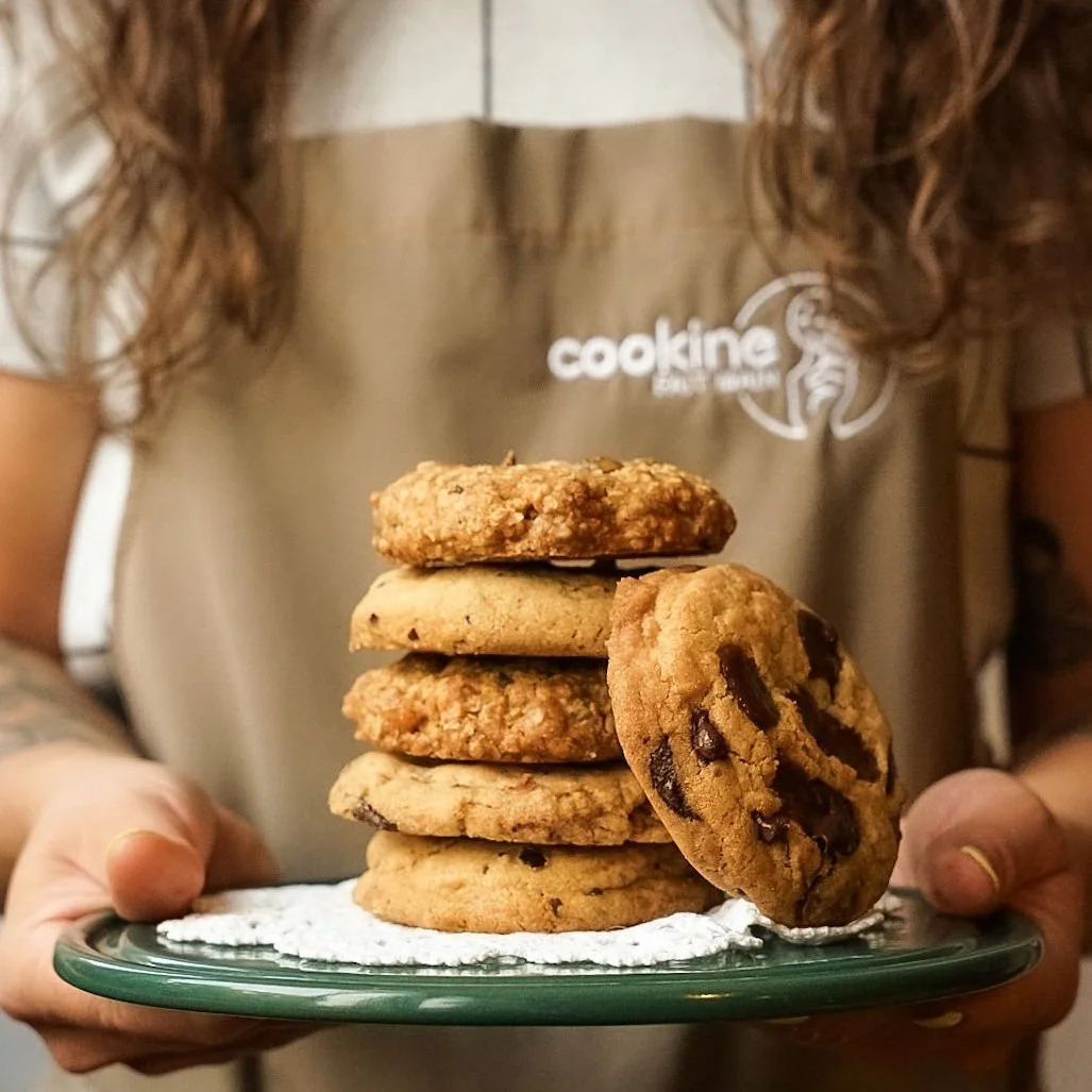 Une personne tient une assiette avec plusieurs cookies, dont un cookies aux pépites de chocolat à côté.