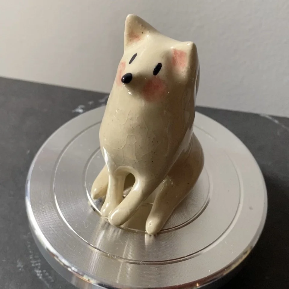 Statue en forme de chien ou animal, de couleur beige avec des joues roses, posée sur un plateau métallique.