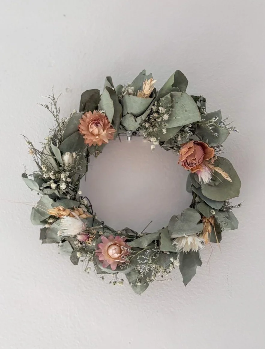 Guirlande de fleurs séchées avec des feuilles vertes et des fleurs roses, blanches et orange, accrochée au mur