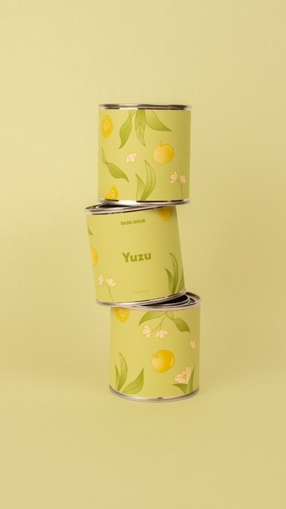 Trois boîtes de conserve empilées en équilibre, la boîte du milieu porte l'inscription "Yuzu" sur un fond vert pastel avec des motifs de feuilles et de fleurs