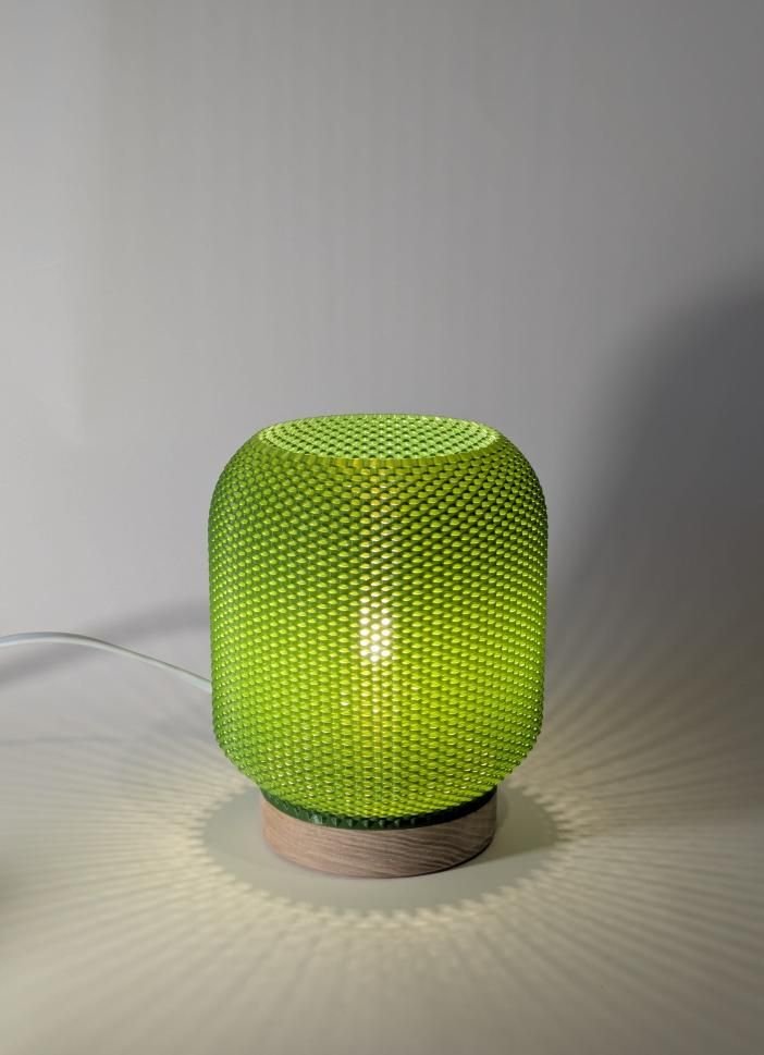 Une enceinte Bluetooth vert vif avec une grille en mesh, posée sur une base en bois, éclairée et branchée par un câble électrique.