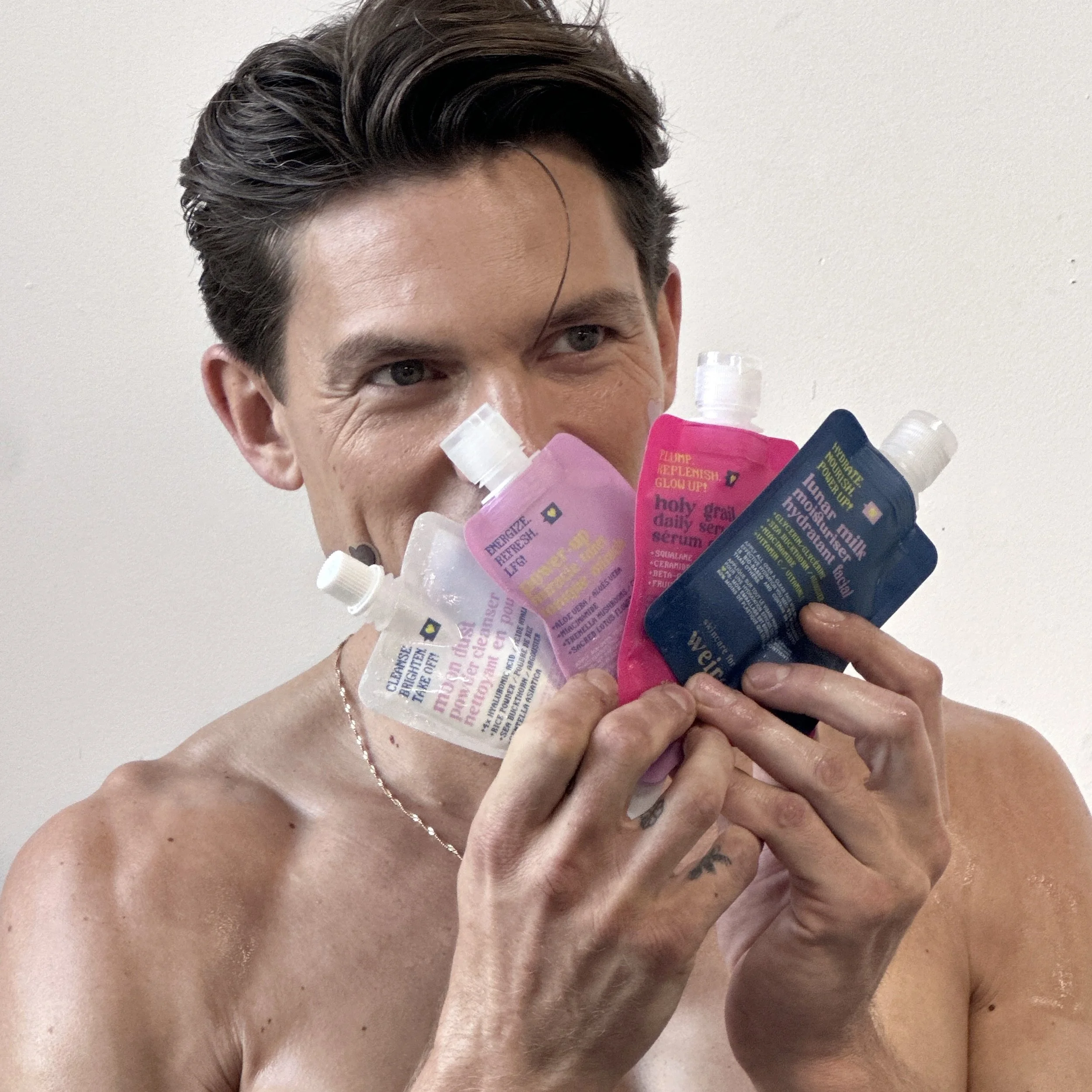 Une personne nue de sexe masculin tenant des tubes de sérum de différentes couleurs près de son visage.