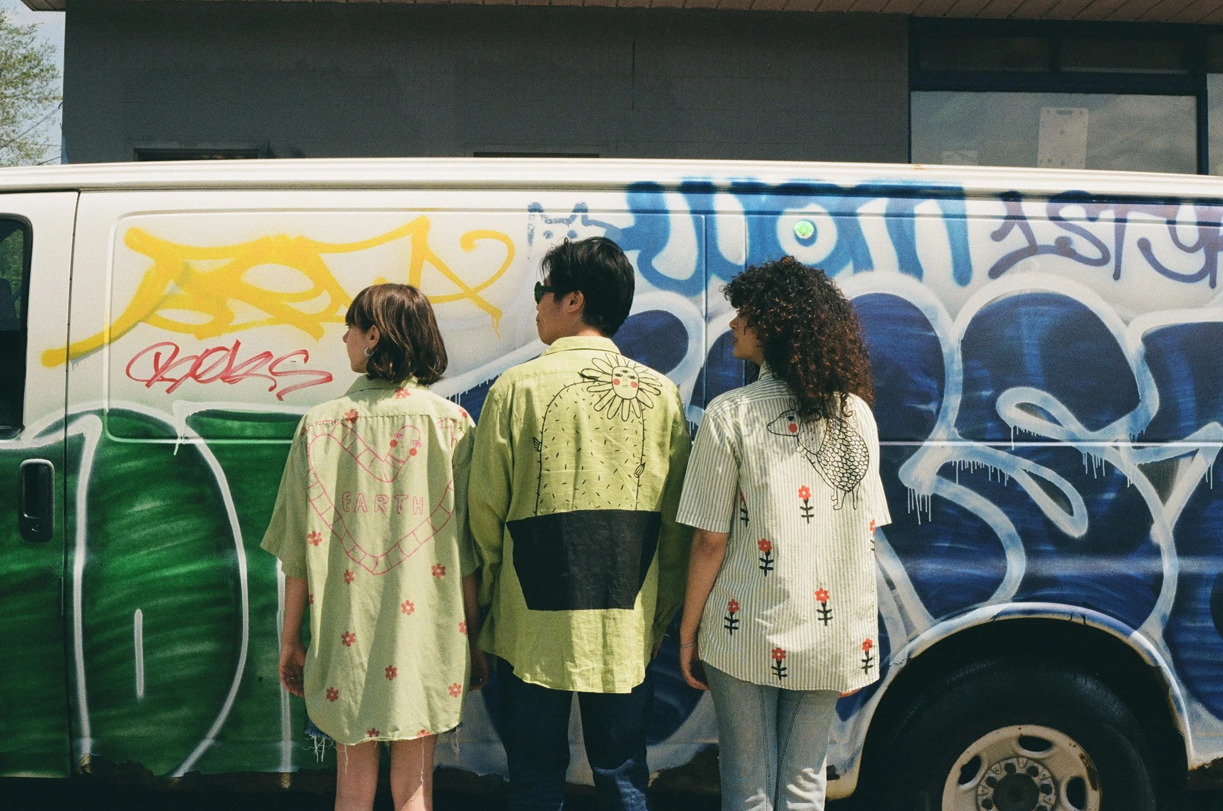 Trois personnes en vêtements imprimés posent devant un camion graffité.