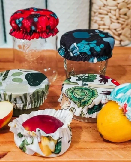 Confitures ou gelées artisanales dans des pots recouverts de tissus colorés avec rubans, placés sur une table en bois avec un fruit jaune et un morceau de pomme.