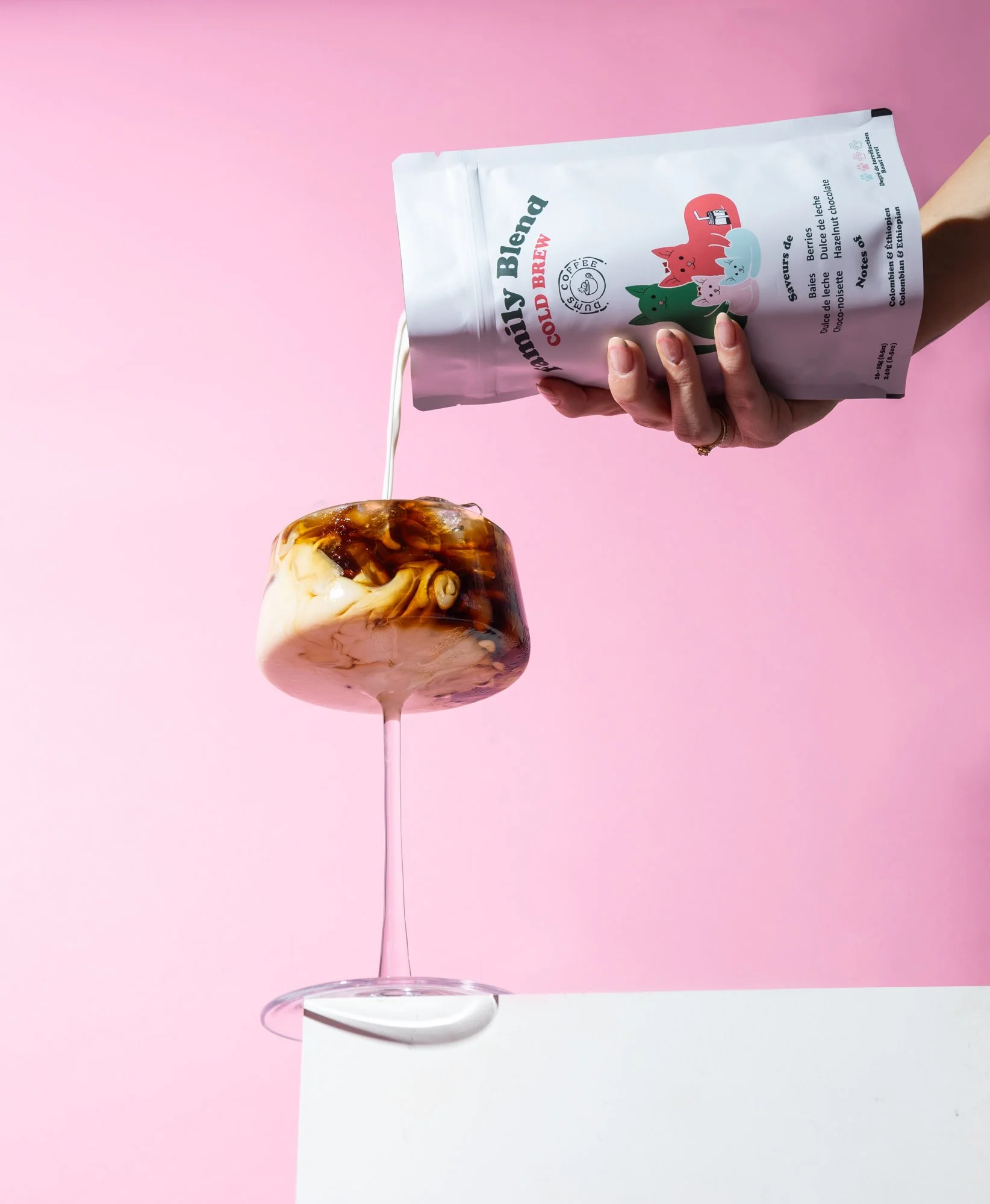 Une main tenant un sac de bonbons à la vanille et caramel, avec une table blanche en dessous et un fond rose