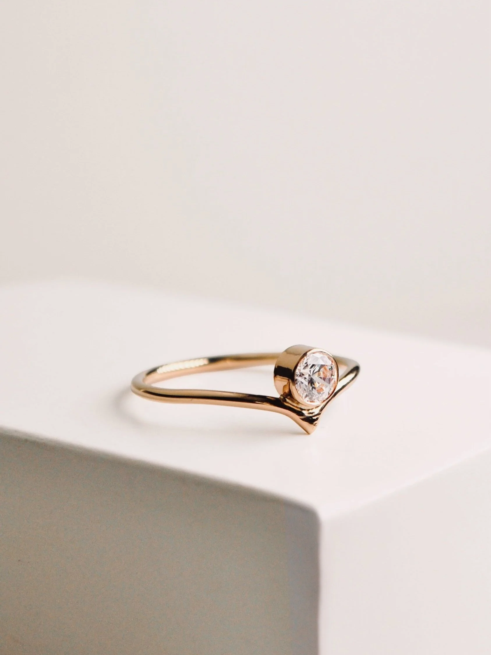 Bague en or rose avec un diamant central brillant, posée sur une surface blanche avec un léger ombrage.