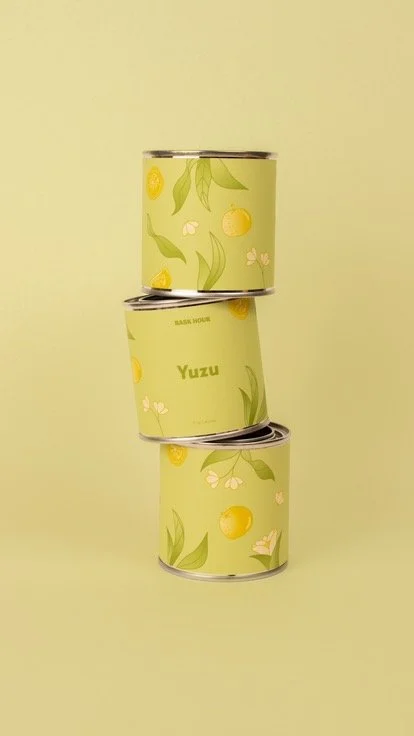 Trois boîtes de conserve vertes empilées en déséquilibre, avec des motifs de citron, de feuilles et de fleurs, avec une légende "Yuzu" sur la deuxième boîte, contre un fond vert clair.