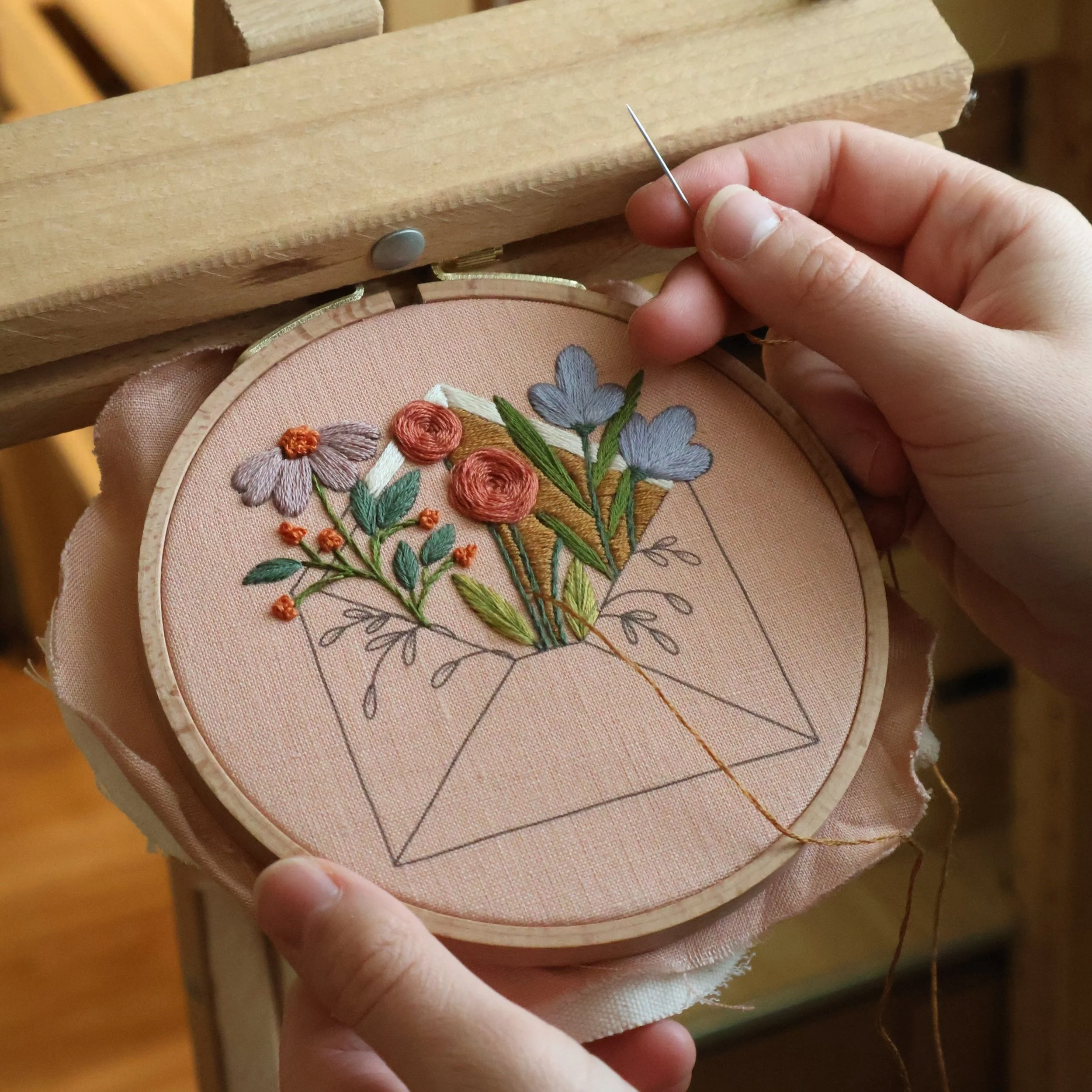 Une main tenant une aiguille près d'une toile de broderie avec des fleurs colorées brodées.