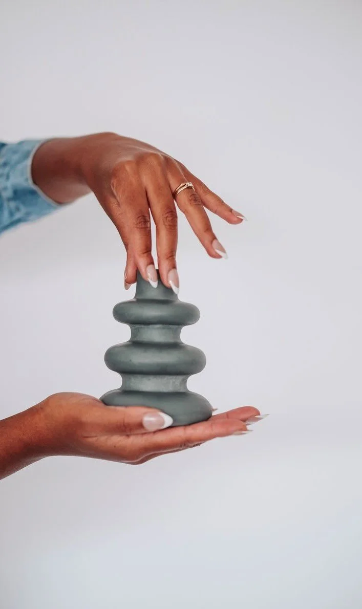 Deux mains tenant une sculpture en forme d'escargot gris.