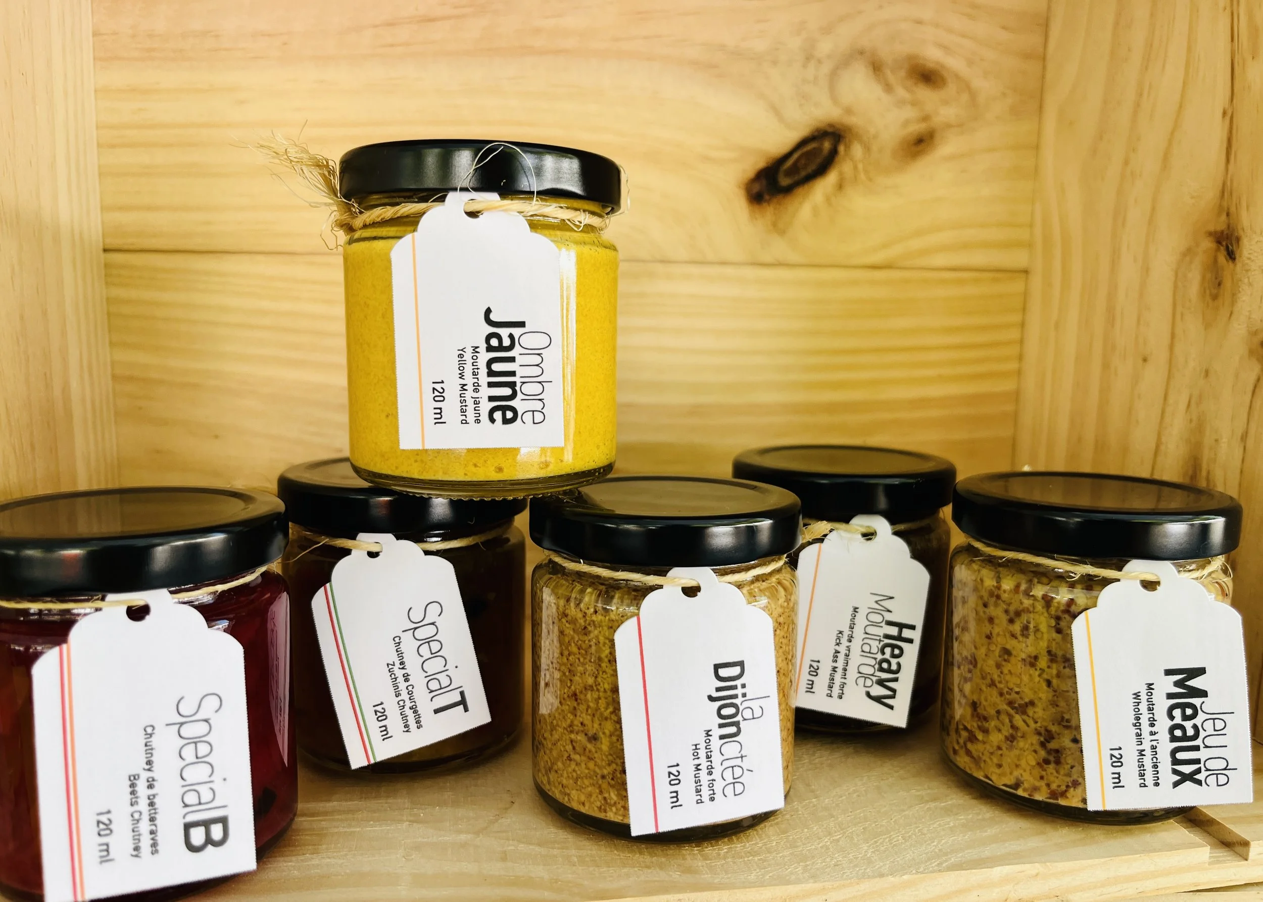Assortiment de bocaux de moutarde à l'ancienne sur une étagère en bois, avec étiquettes en français.
