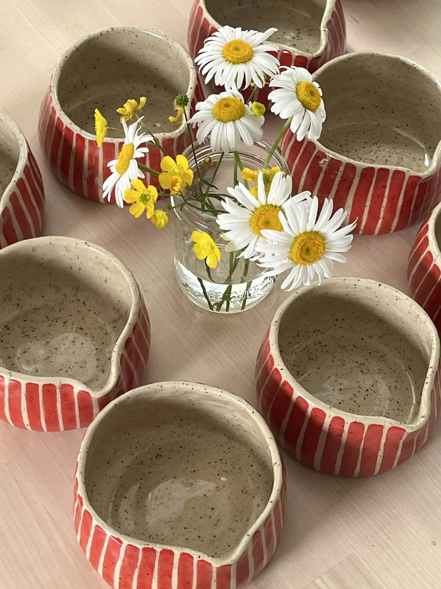 Keramisks vases with red and white stripes, filled with a bouquet of daisies and yellow flowers, placed on a wooden surface.