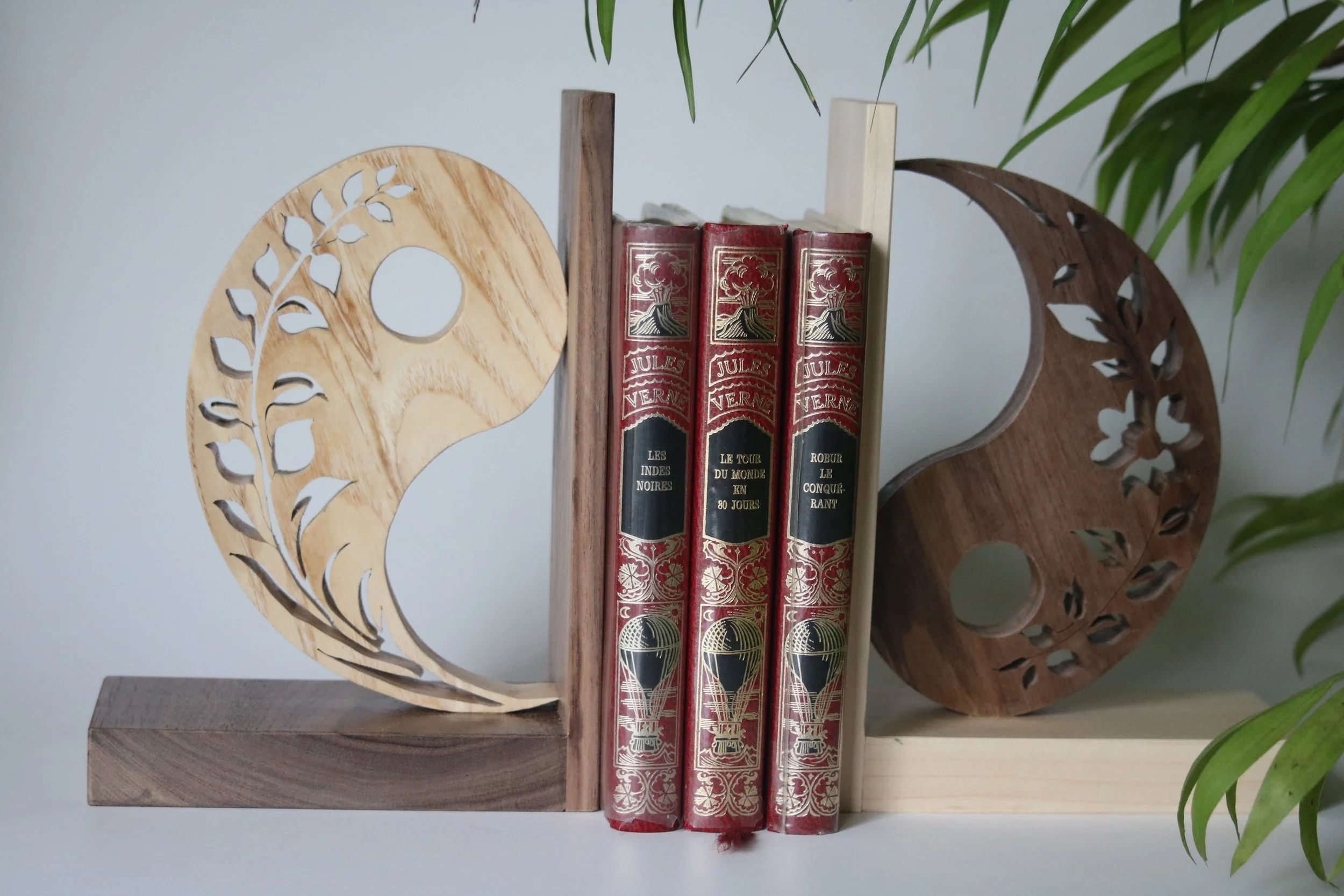 Une étagère en bois avec deux décorations en forme de tête de lion en bois, une sur chaque côté, et trois livres rouges au centre, placés verticalement.