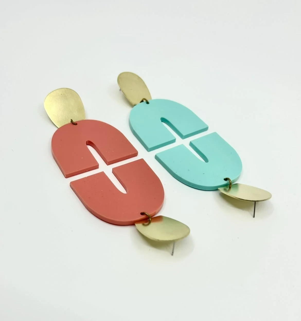 Deux grands boucles d'oreilles colorées en forme de lettres 'E' et 'G' avec des éléments en métal doré attachés en haut et en bas.