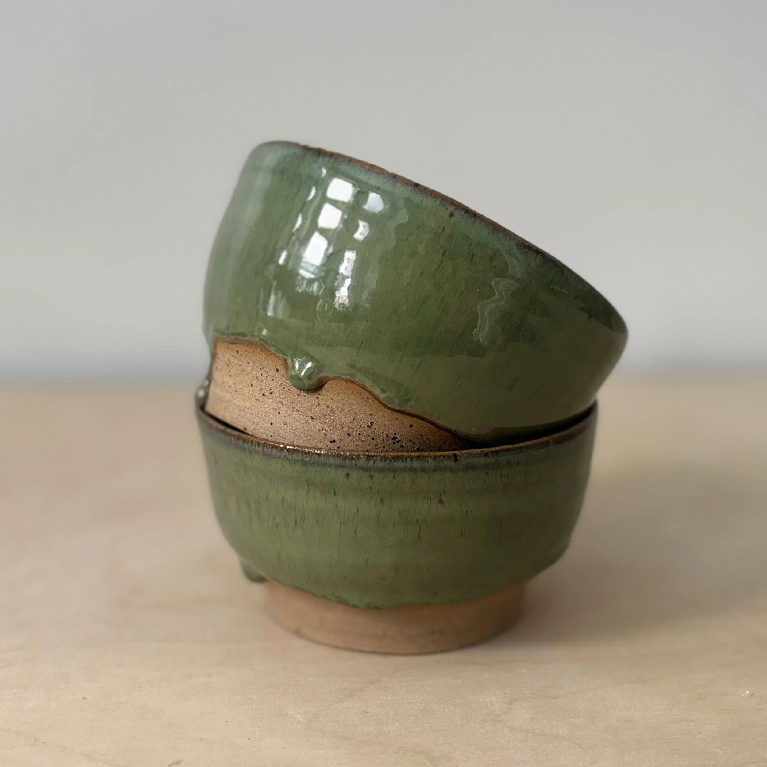 Une coupe en céramique verte avec un motif en grille près du bord, vue de côté, posée sur une surface claire.
