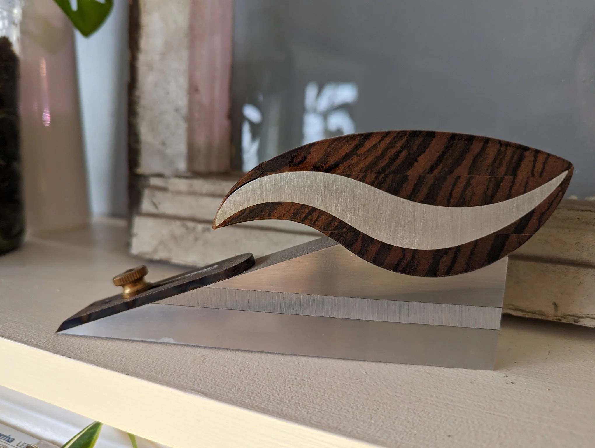 Une cuillère en bois avec un manche courbé en design décoratif, posée sur une surface blanche. En arrière-plan, il y a un mur gris et une surface en pierre ou en béton.