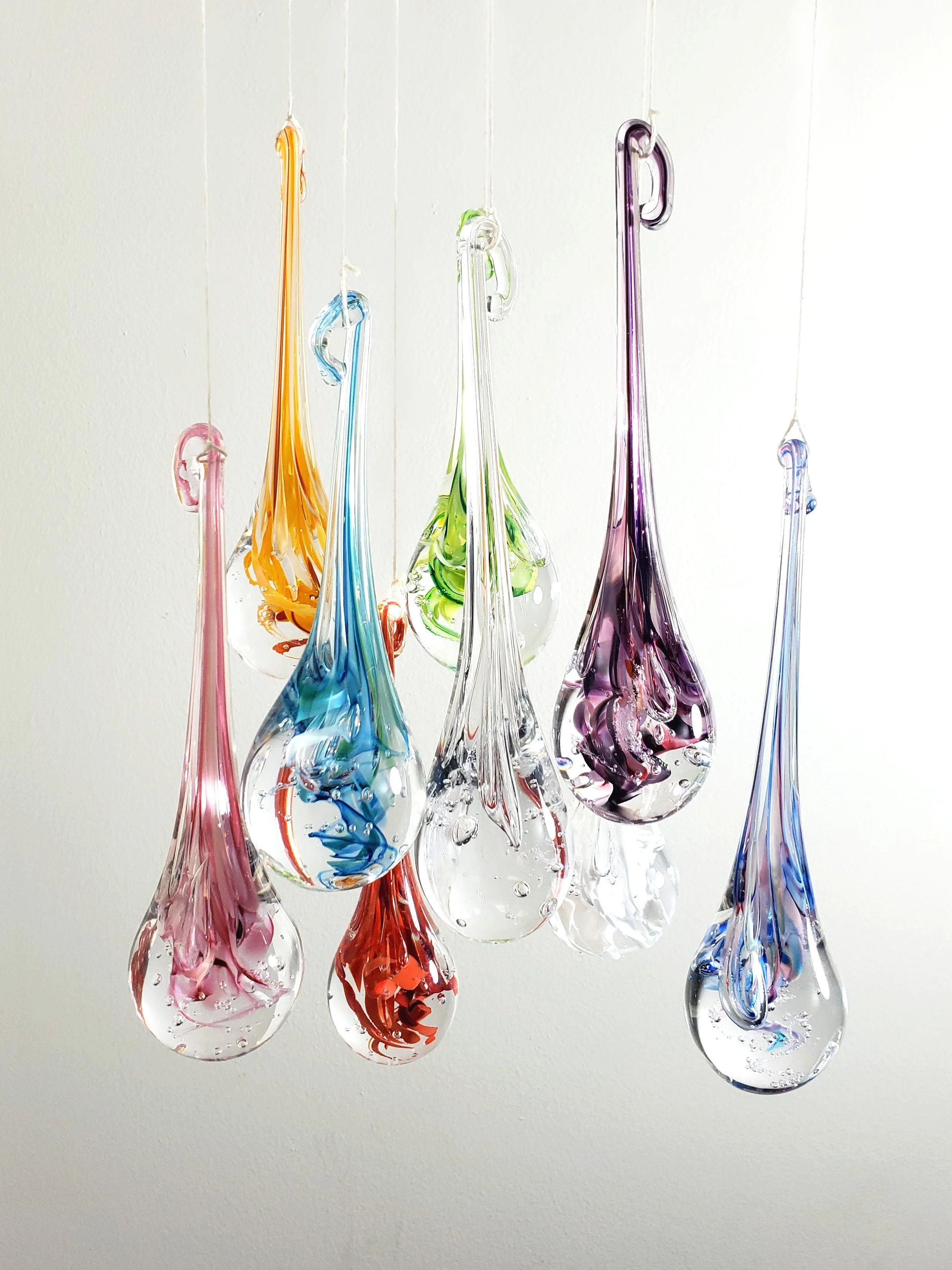 Suspensions en verre soufflé de différentes couleurs et formes, suspendues contre un fond blanc.