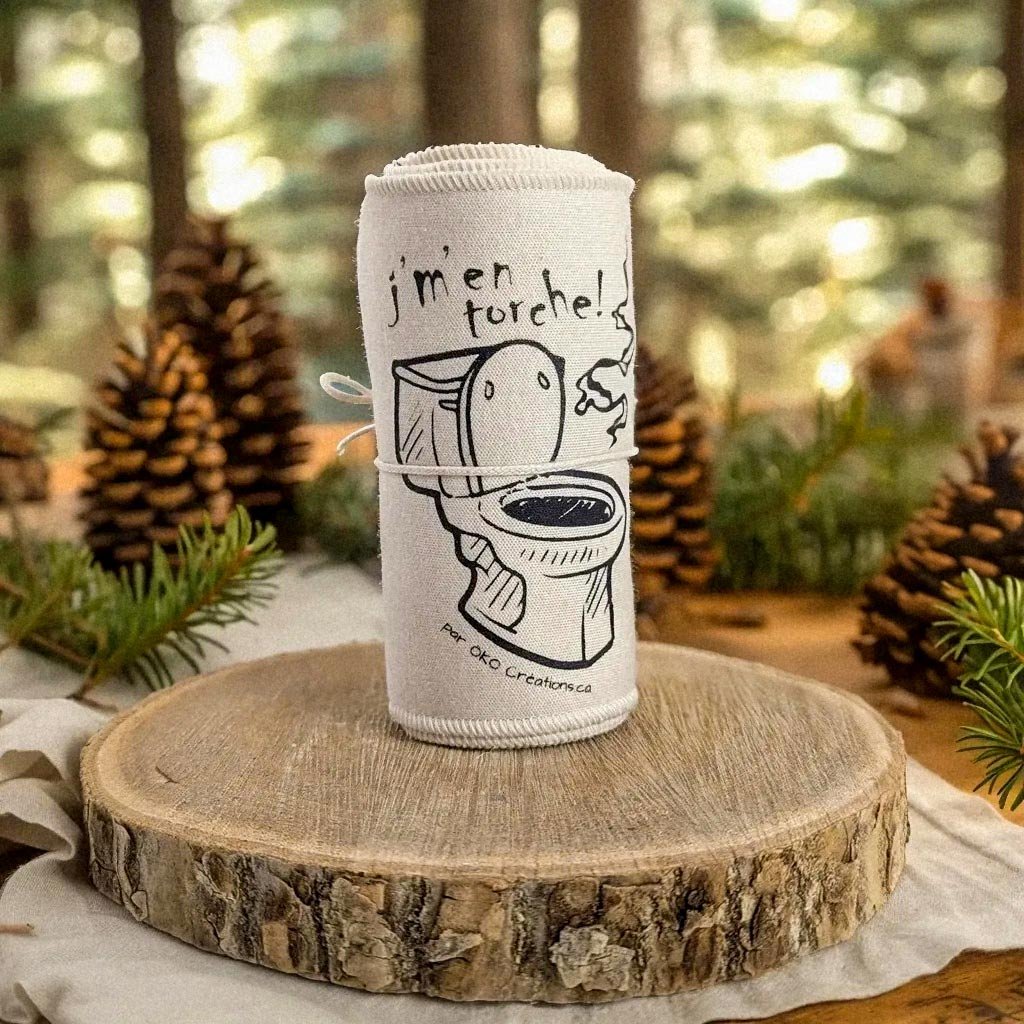 Un rouleau de papier toilette avec une illustration humoristique de toilettes et un dessin d'une cuillère, avec le texte "j'm'en fout!" écrit dessus, placé sur une surface en bois, avec un décor de forêt en arrière-plan.
