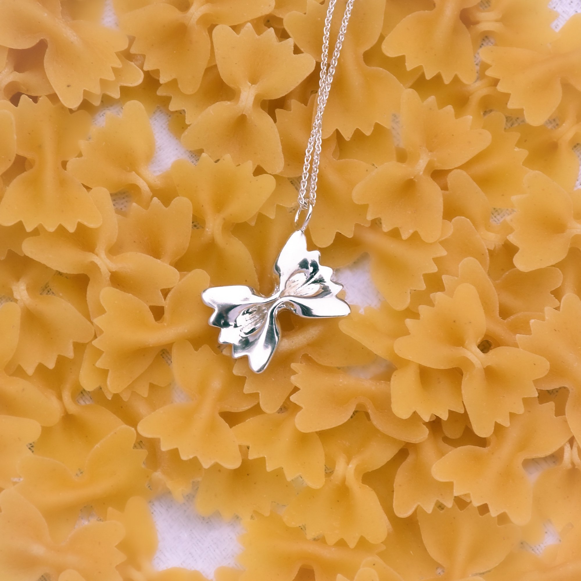 Une chaîne en argent avec une pendentif en forme de feuille est posée sur un lit de pâtes farfalle.