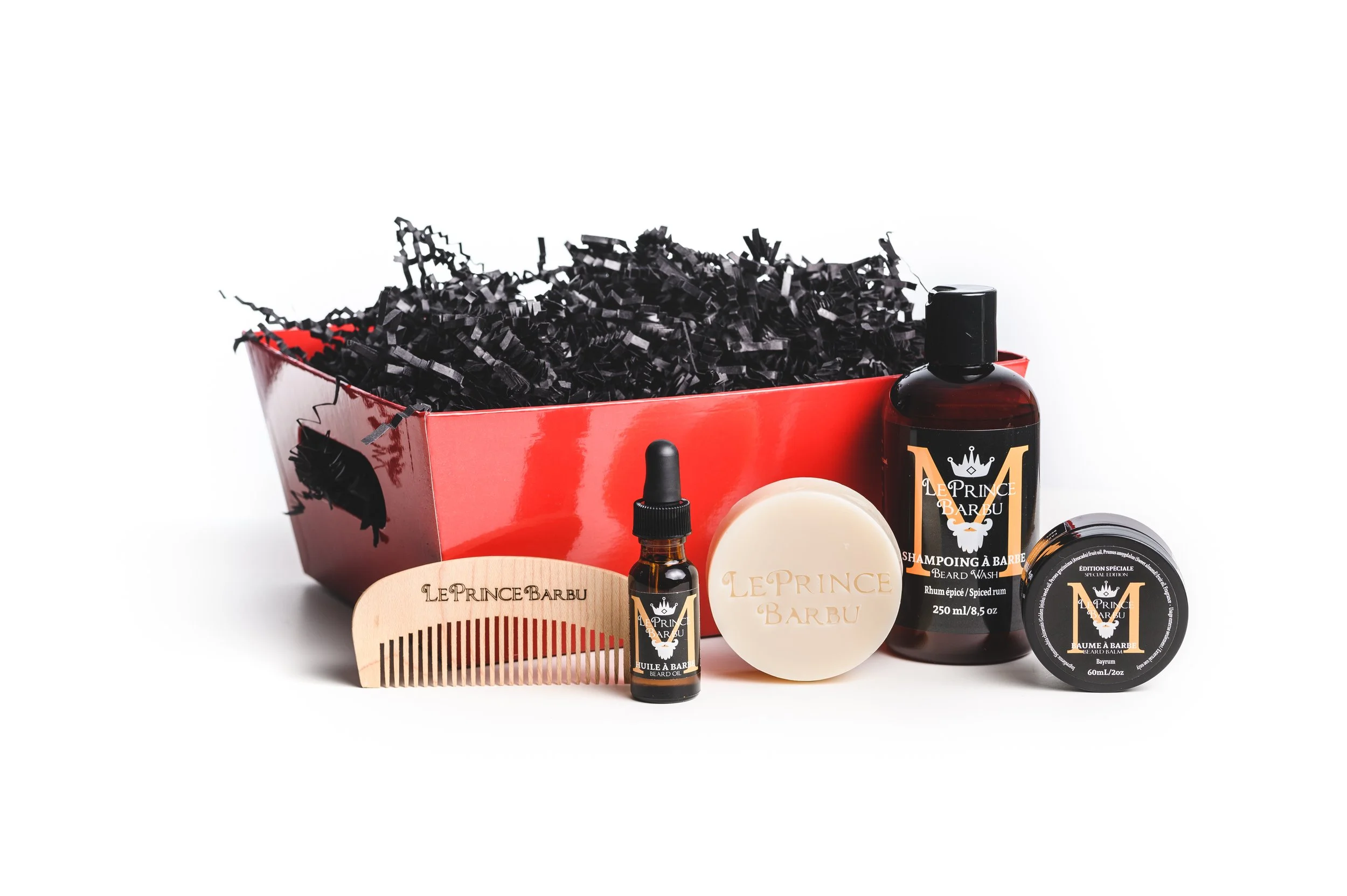 Un coffret rouge contenant des produits pour l'entretien de la barbe, notamment de l'huile, un shampooing, un savon et une brosse à barbe, sur fond blanc.
