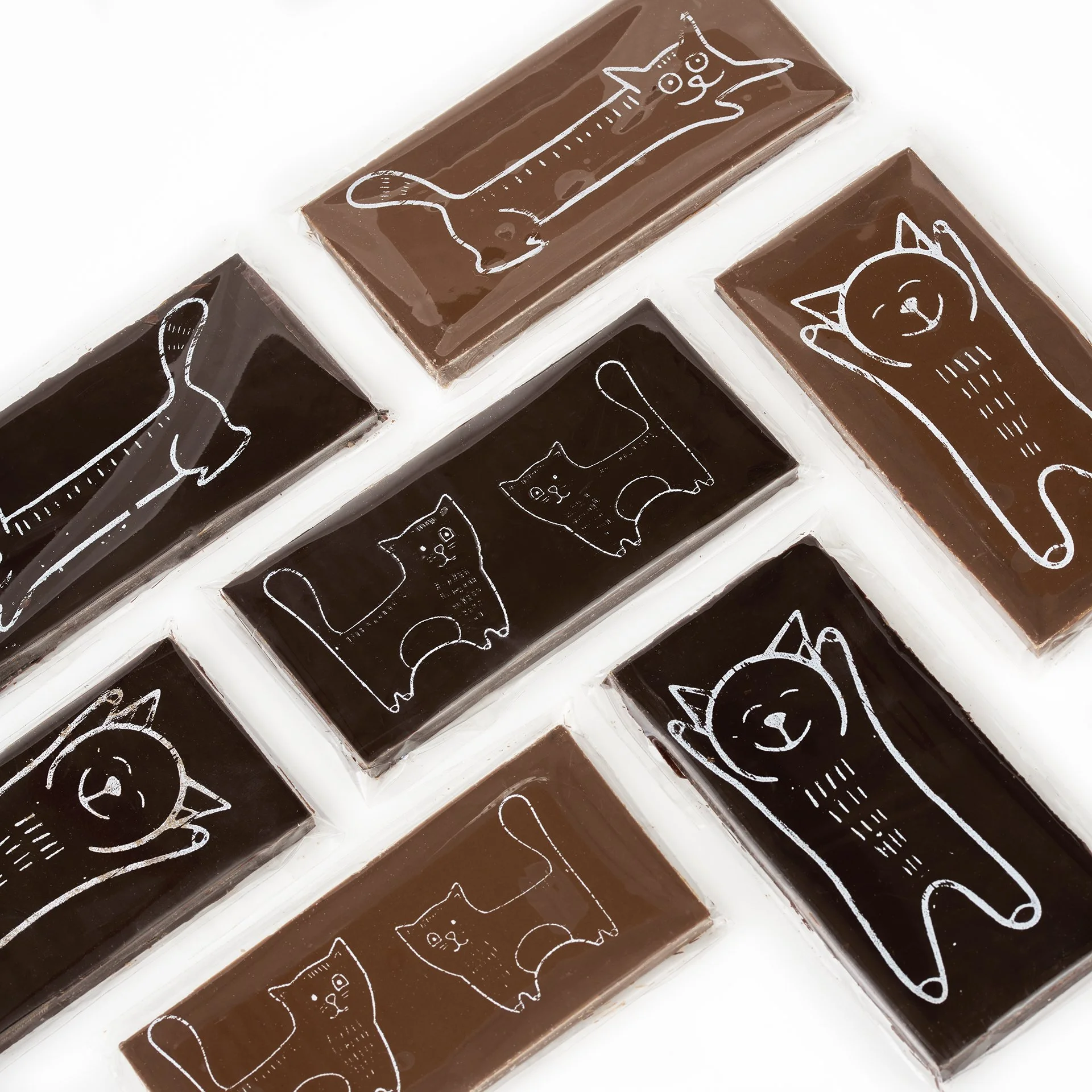Tablettes de chocolat illustrées avec des dessins de chats en style sculpture blanche sur un fond marron et noir.