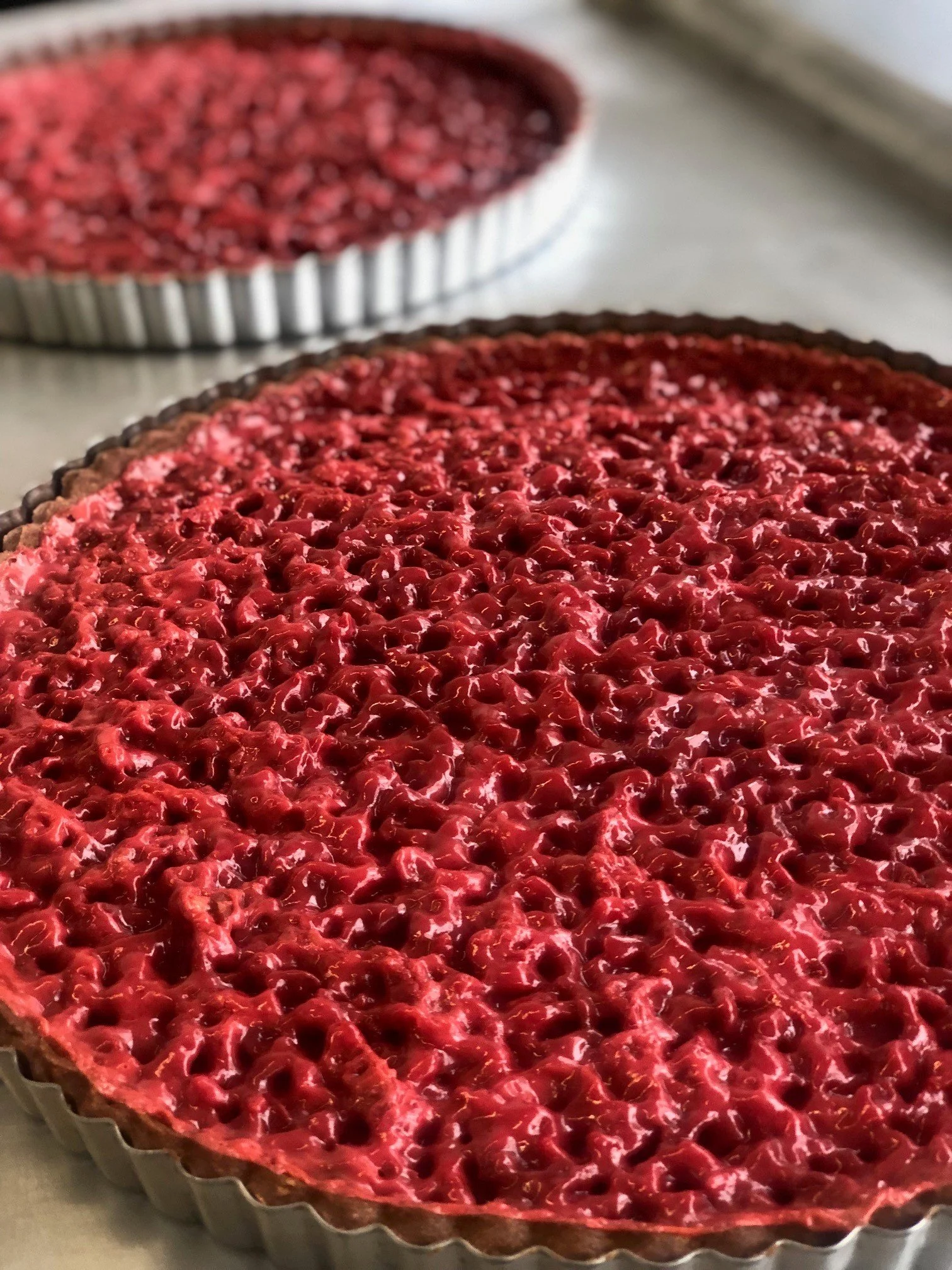 Tarte aux fruits rouges dans un moule, avec une garniture de cerises, fraises et autres fruits rouges, sur une surface en argent.