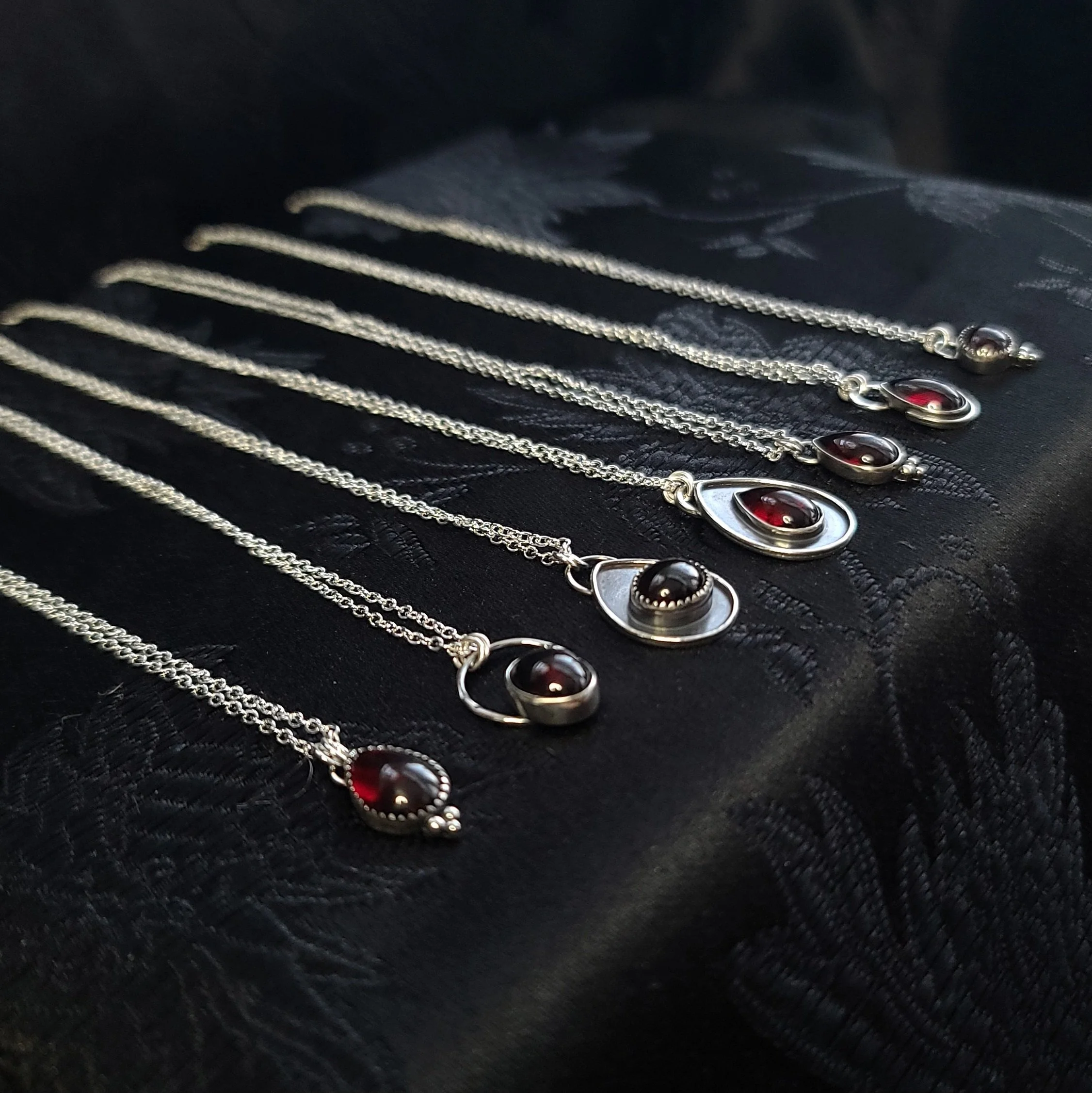 Une série de colliers en chaîne avec des pendentifs en forme d'œil rouge, alignés sur du tissu noir.