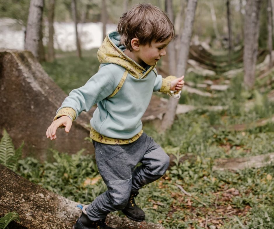 Un garçon qui court dans une forêt, portant un sweat à capuche et des pantalons de randonnée.